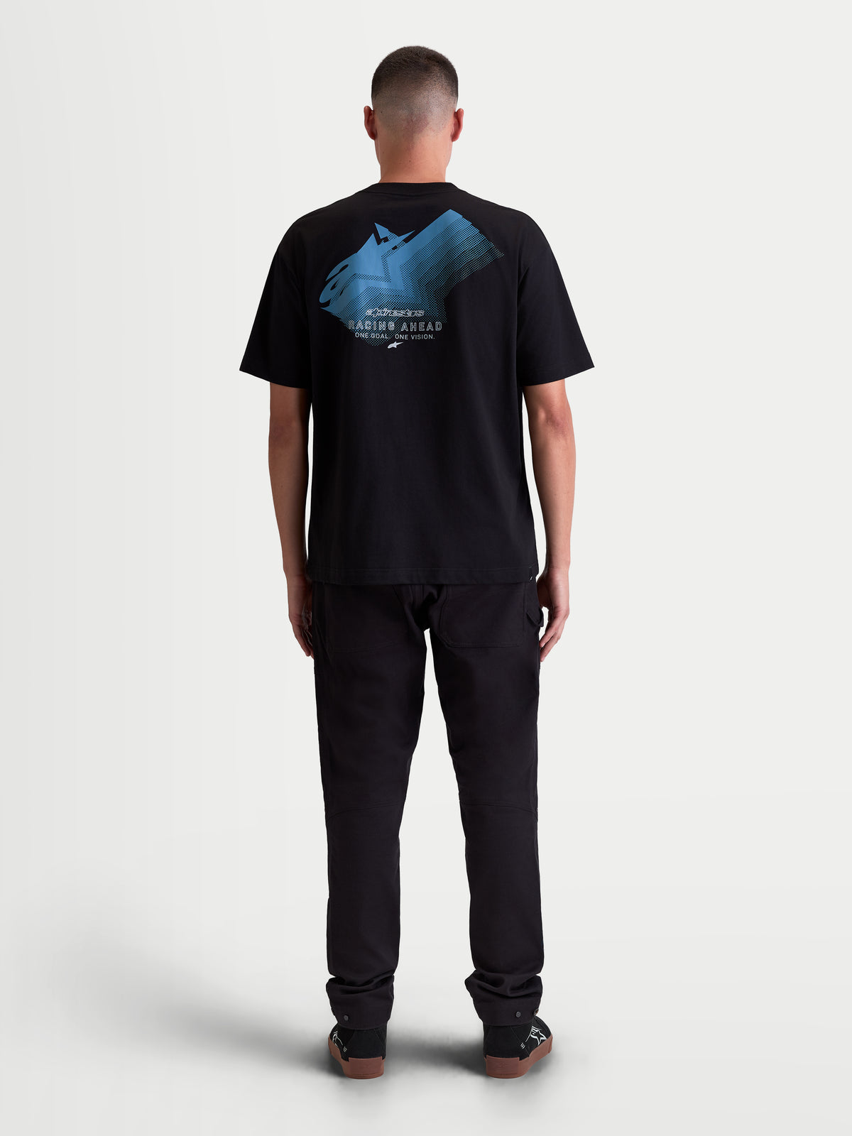 Alpinestars Ghost Oversized CSF T-Shirt, zwart heren T-shirt met korte mouwen, blauwe fade logo-graphic op de rug met 'Racing Ahead' en 'One Goal. One Vision.' tekst, relaxte oversized pasvorm, motorsport-geïnspireerde lifestyle kleding, achteraanzicht op model.