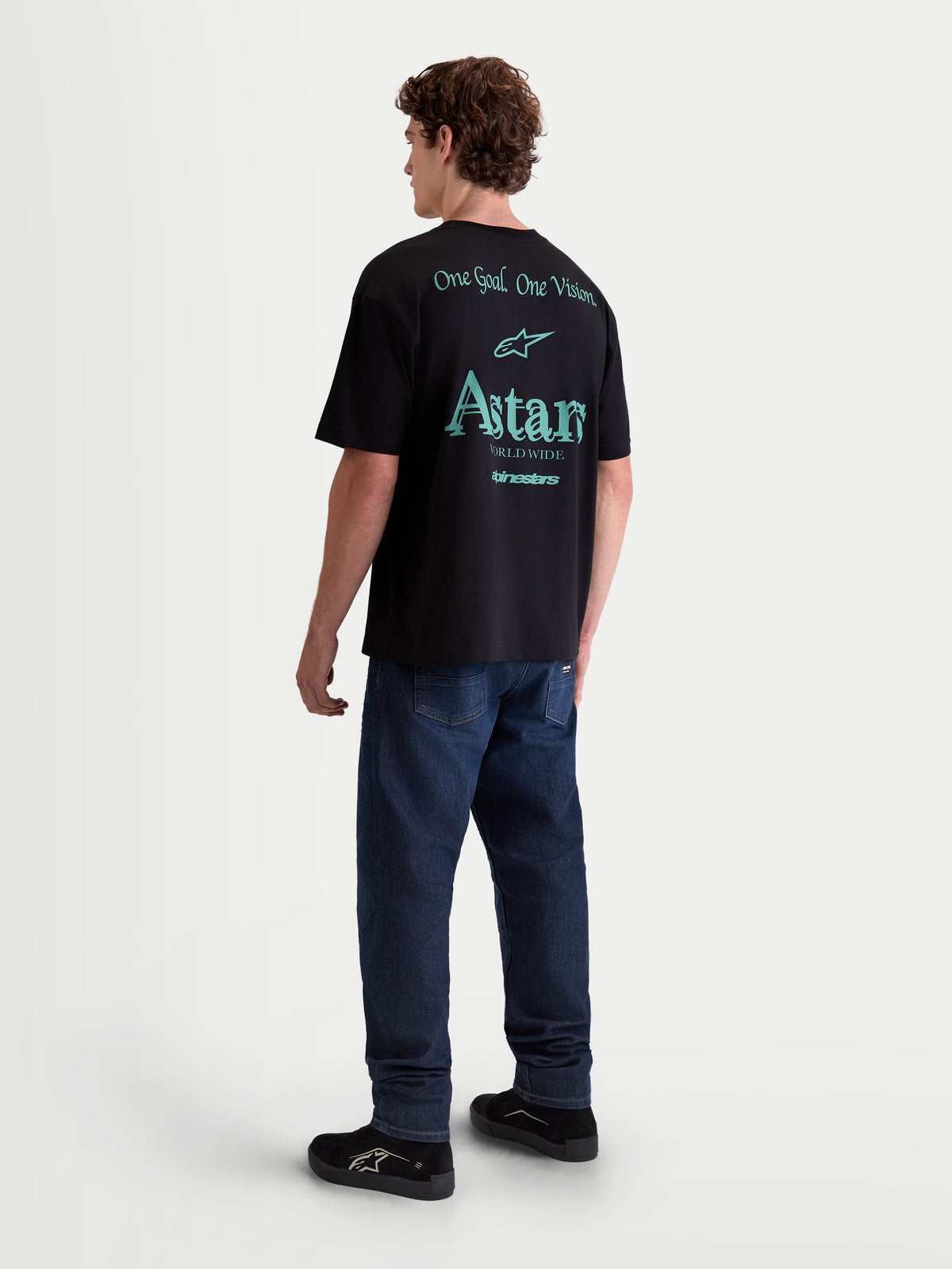 Alpinestars Post Oversized CSF T-shirt, heren-lifestyle-sportswear, zwart met blauwgroene graphics op de achterzijde, achteraanzicht op model, met One Goal One Vision en Astars Worldwide tekst, zachte katoenmix.