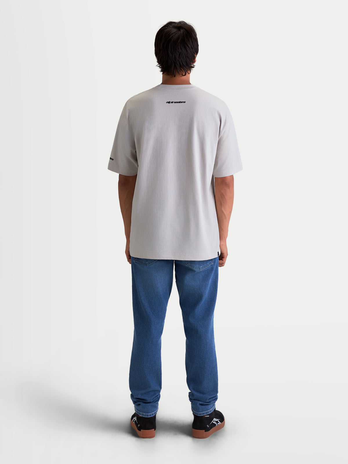 Alpinestars Mandate Oversized CSF T-shirt, unisex sportswear t-shirt met korte mouwen, grijs, achteraanzicht op model. Ontspannen oversized pasvorm met een zwarte Alpinestars-woordmerkgraphic op de bovenrug, gemaakt van een zachte katoen-polyestermix voor dagelijks comfort.