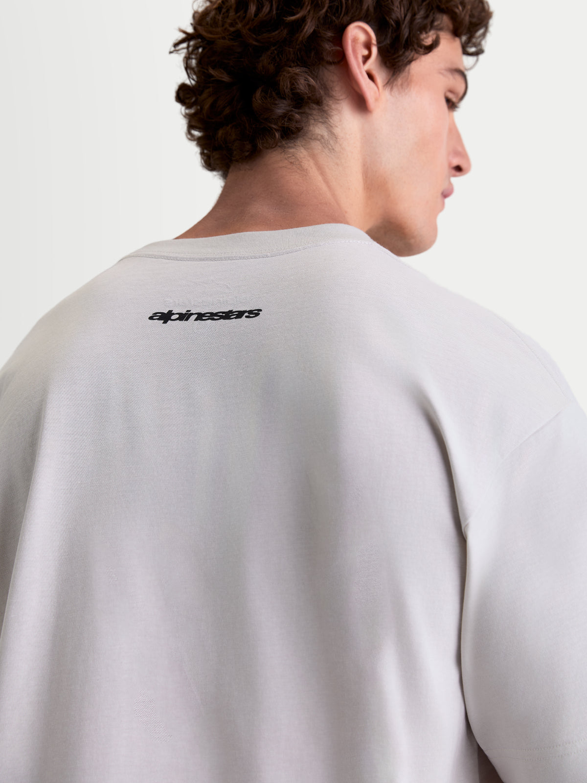 Alpinestars Prelude Oversized CSF t-shirt, sportswear t-shirt met korte mouwen, cementgrijs en zwart, achteraanzicht op model met Alpinestars-woordmerk op de rug, relaxed oversized pasvorm, katoen-polyestermix.