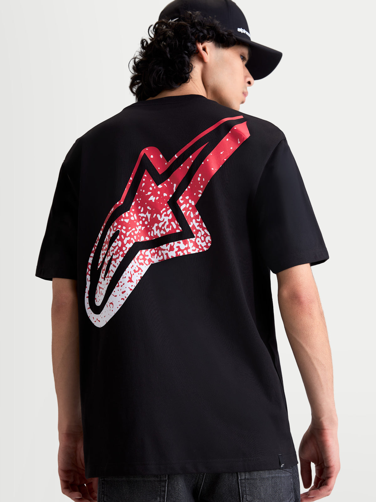 Alpinestars Meteor CSF t-shirt met korte mouwen, zwart, achteraanzicht op model met een groot rood en wit MX-geïnspireerd Astars-logo met kleurverloop op de rug, casual motorsportkleding.