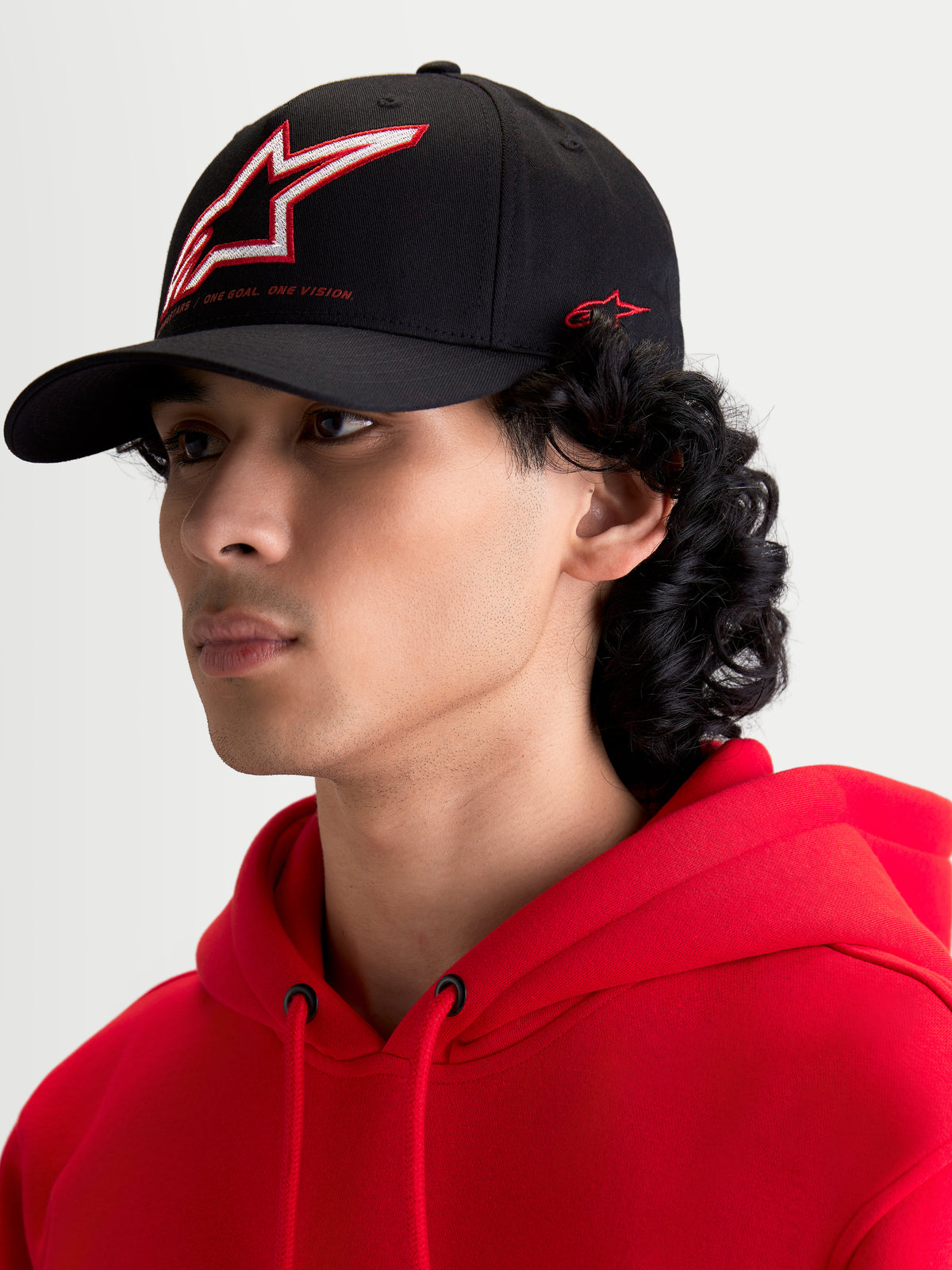 Alpinestars Lineout pet, zwarte sportswear baseballpet met gebogen klep, voorzien van een gestructureerde kroon met rood en wit geborduurd Astars-logo en branding aan de zijkant, getoond op een model.