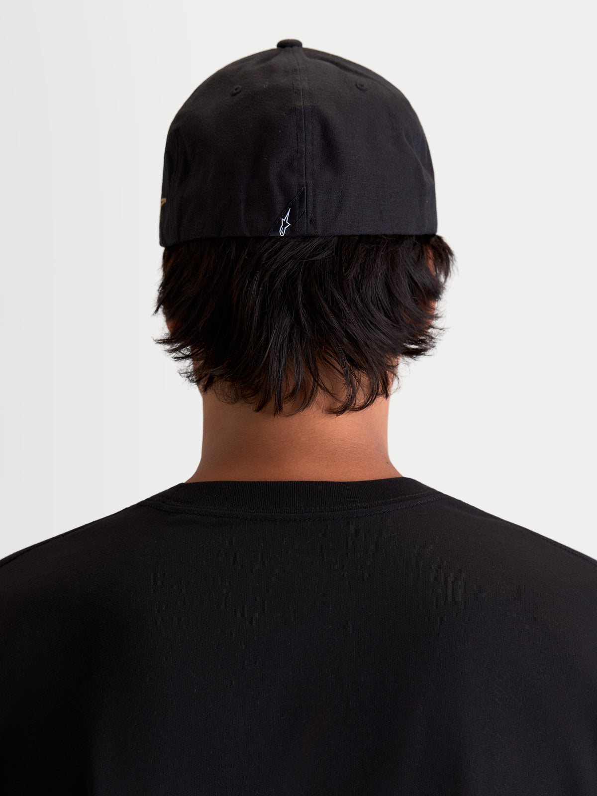 Alpinestars County Canvas pet, zwarte sportswearpet, achteraanzicht op model, flex-back-pasvorm met klein geborduurd Astars-logo op de achterzijde, oxford peached canvas voor dagelijks comfort.