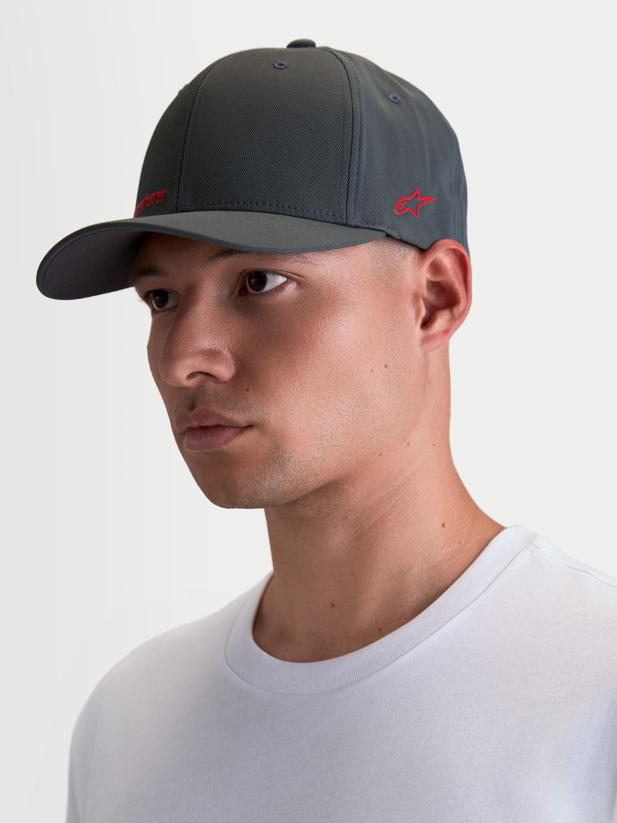 Alpinestars Points pet, sportswearpet met gebogen klep op model, donkergrijs en rood, lichtgewicht nylon tactel, flex-back pasvorm voor dagelijks comfort op en naast de motor.