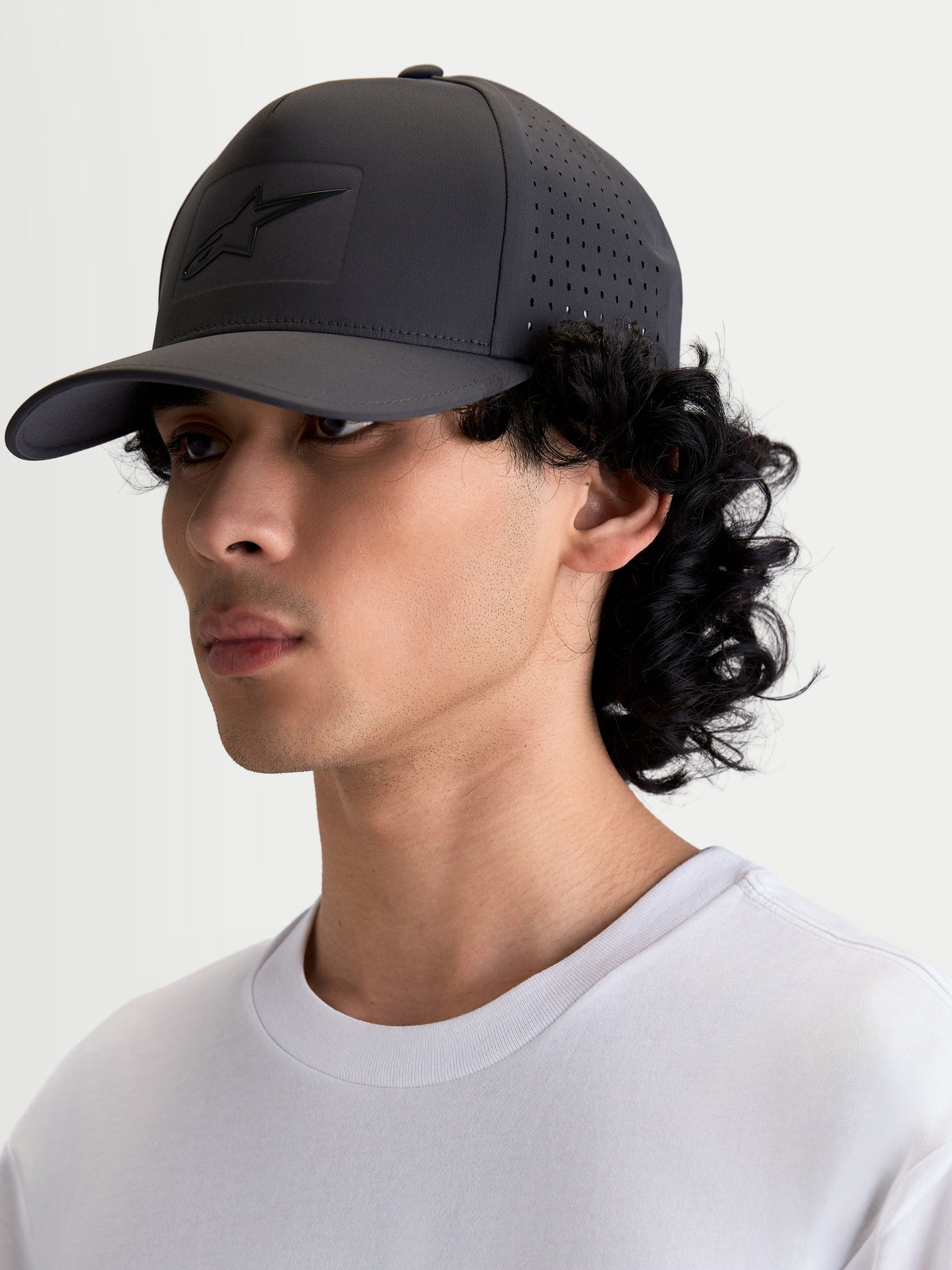 Alpinestars Algo Perf verstelbare pet, sportieve snapback in donkergrijs, zijaanzicht op model met zijperforaties voor luchtstroom, technische stof, sonic-weld logo en gebogen klep.