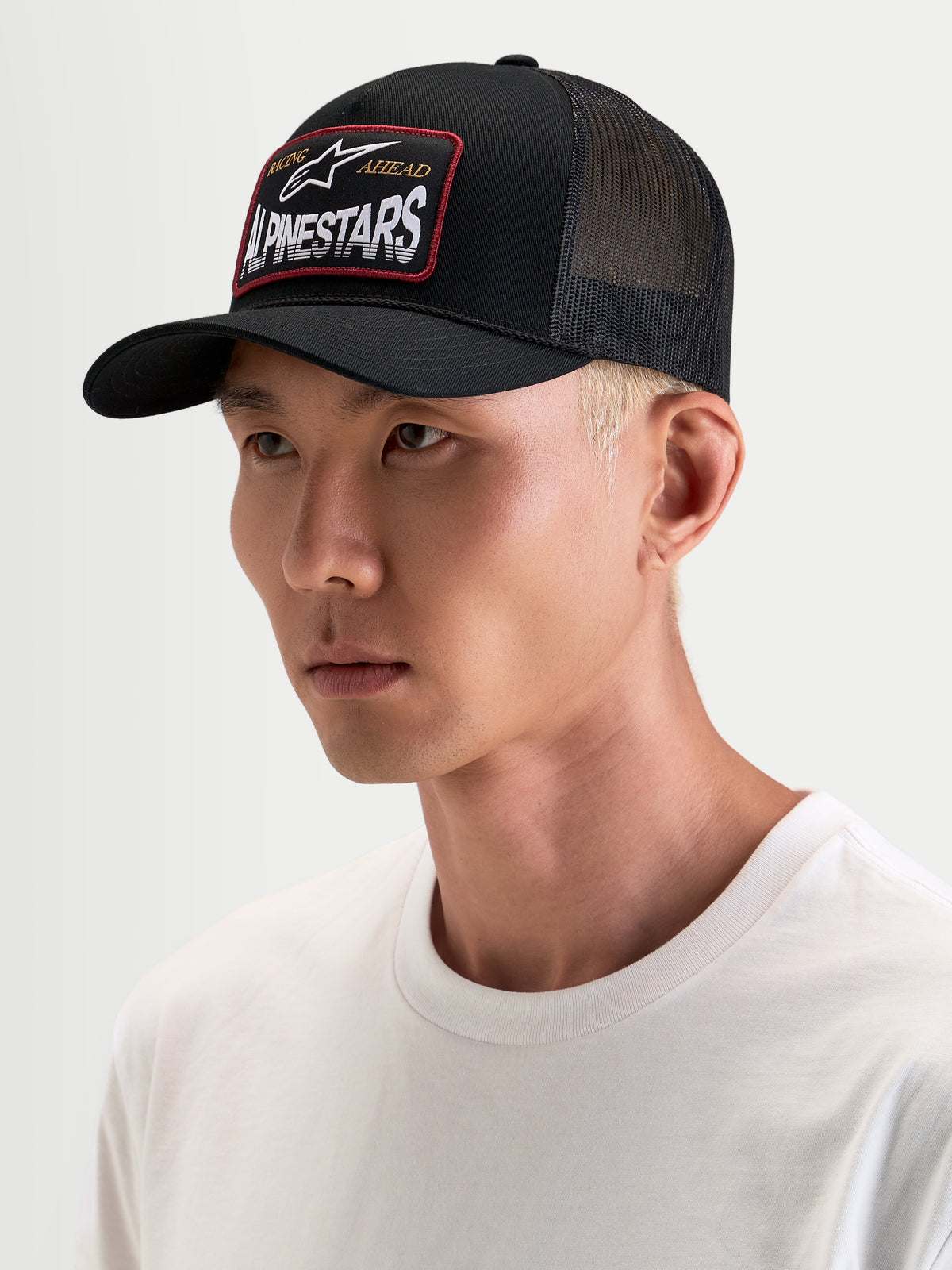 Alpinestars Hemmings Trucker pet, zwarte sportswear snapback pet gedragen door een model, met ademende poly mesh achterpanelen en een geweven Alpinestars-logopatch op de voorkant