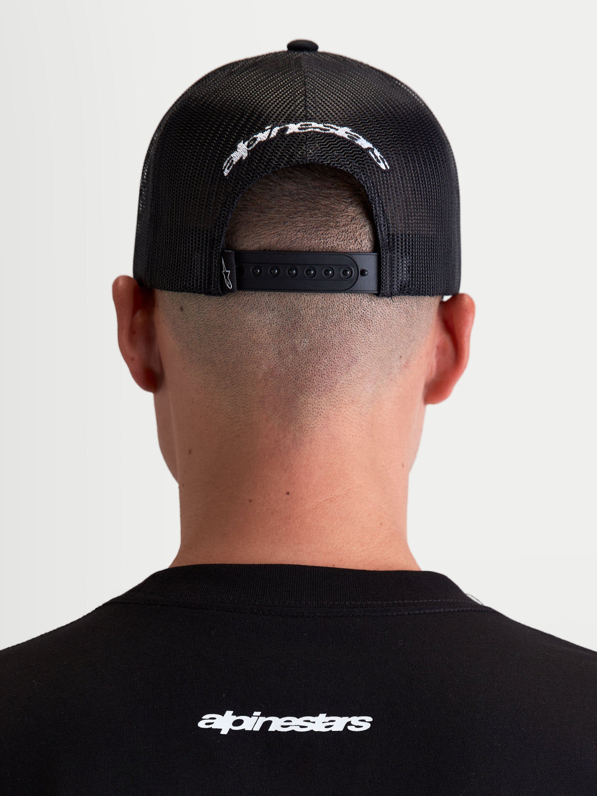 Alpinestars Meteorite Trucker pet, casual sportswear pet met mesh achterzijde, zwart en wit, voorzien van een verstelbare snapbacksluiting en wit geborduurd Alpinestars-logo op de achterzijde, achteraanzicht op model.