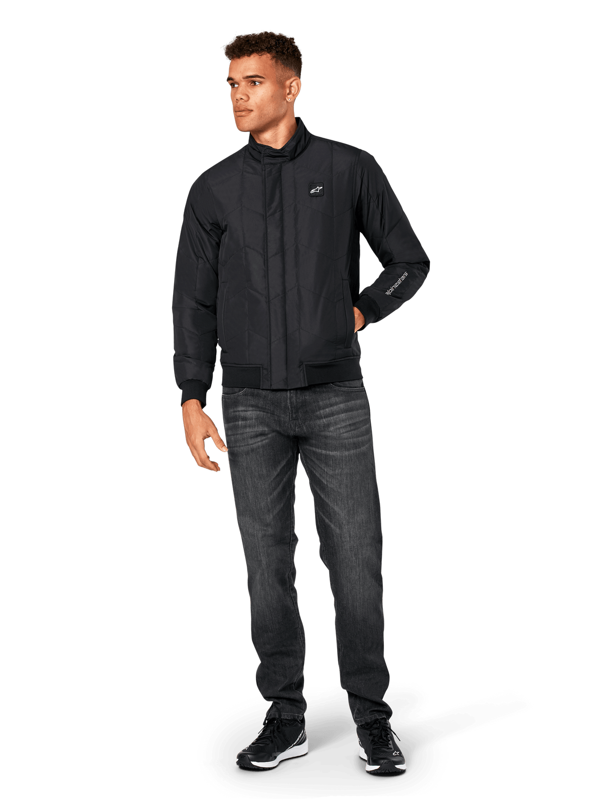 Alpinestars Precedent Jacket, Quilted Sportswear Jacket, Black, worn with dark grey jeans and black sneakers, featuring an angled quilt pattern, low track collar, rib-knit cuffs and hem, with a white logo patch on the chest and sleeve embroidery.