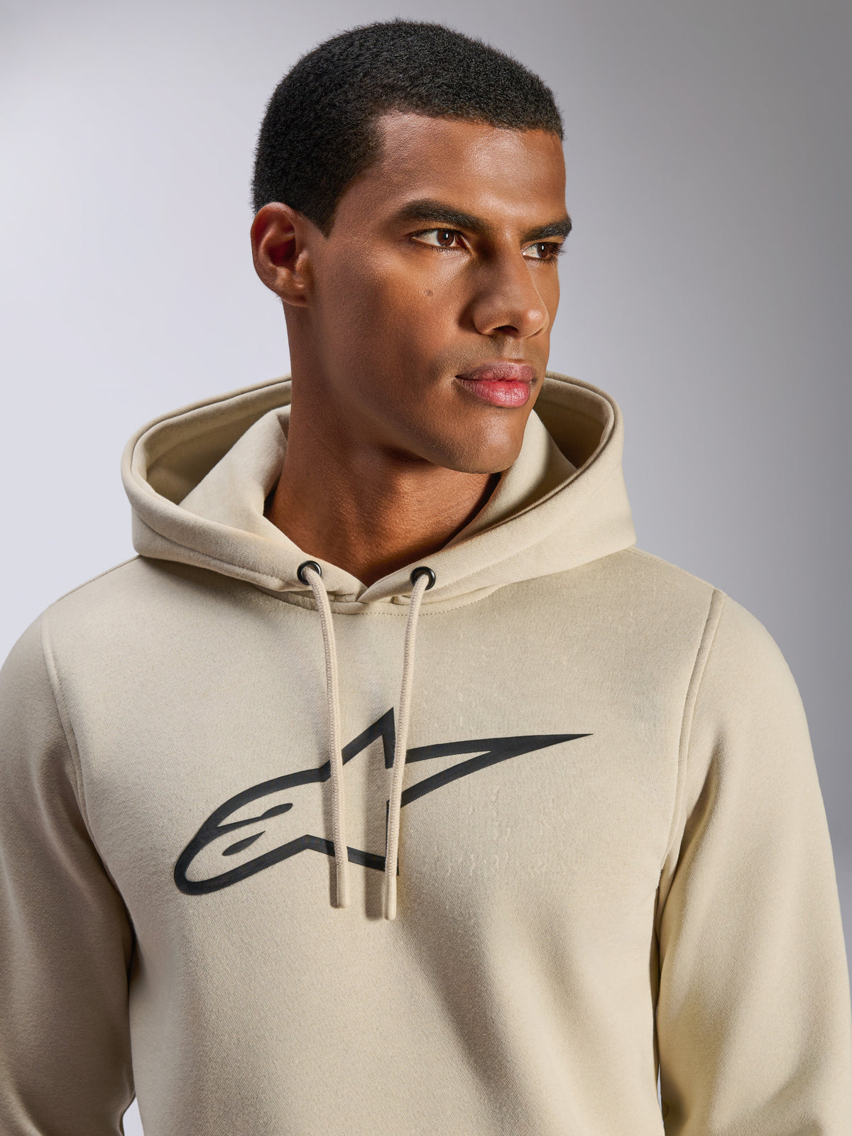 Alpinestars Ageless V3 hoodie, casual sportkleding, gebroken wit met zwart geborduurd Alpinestars-sterlogo, capuchon met trekkoord, close-up op model, zachte fleece, modern op de motorsport geïnspireerd ontwerp
