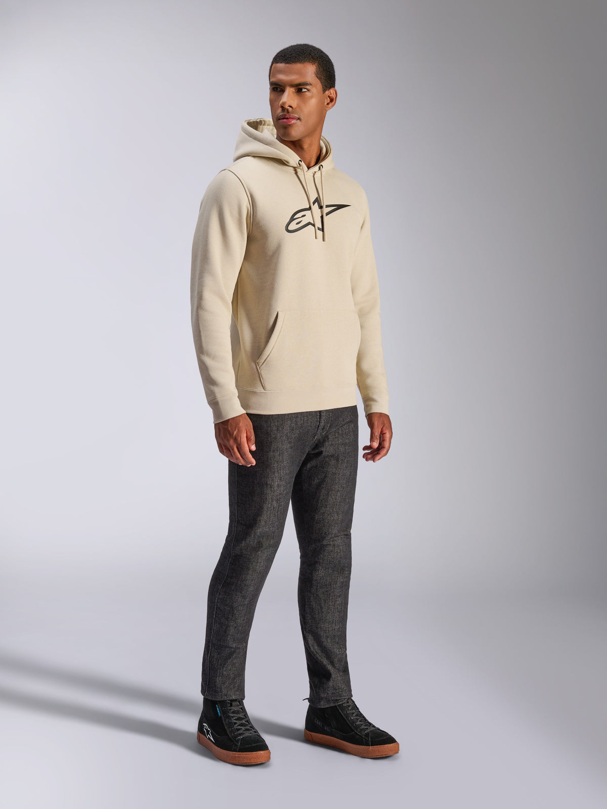 Alpinestars Ageless V3 Hoodie, casual streetwear, Off White met zwart geborduurd logo, fleece hoodie met capuchon, lange mouwen, kangoeroezak aan de voorkant, gecombineerd met een donkere jeans en zwarte sneakers