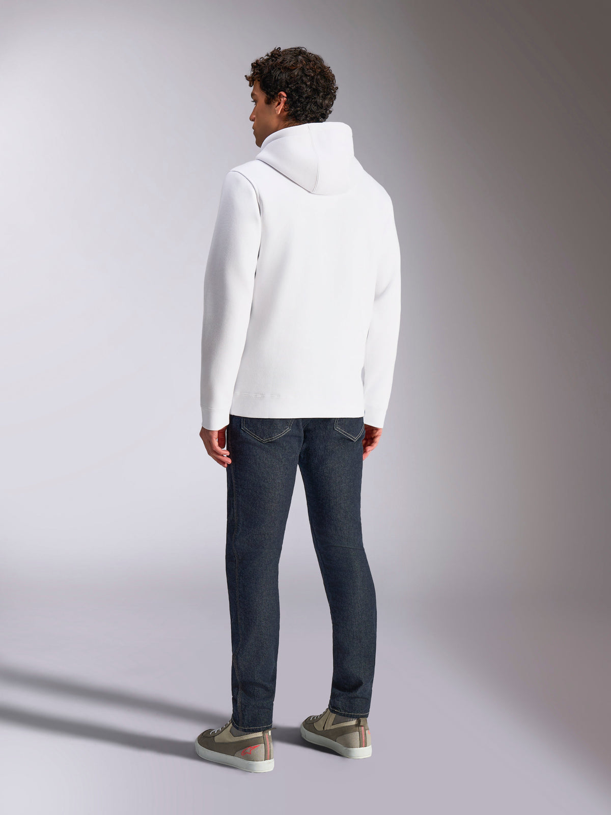 Alpinestars Blaze V3 Hoodie, back view of male model wearing a white pullover hoodie, casual sportswear styled with dark blue jeans and grey sneakers, modern motorsport-inspired design
