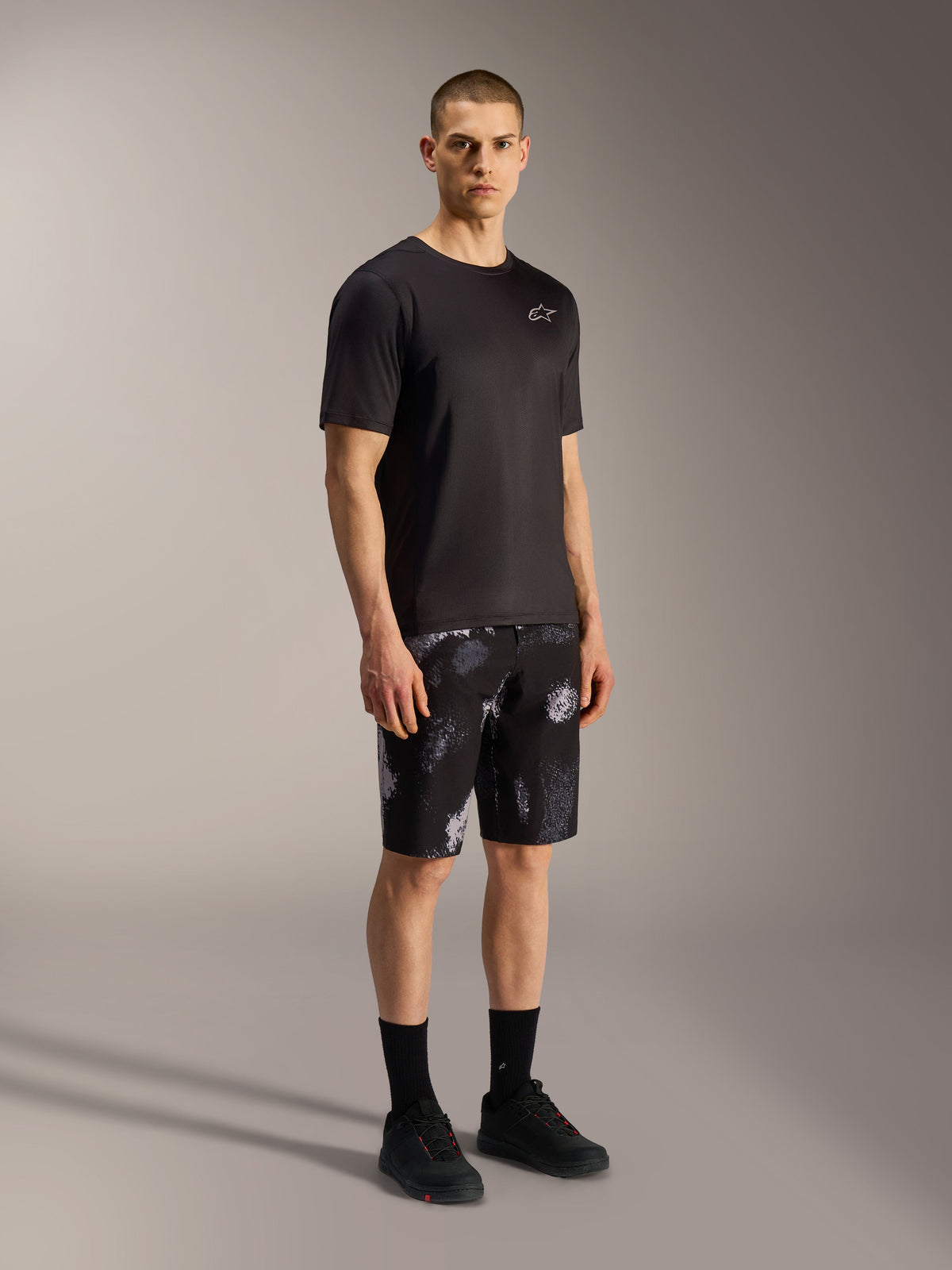 A-Dura Ride MTB-shorts in Black Camo met grijs camouflagepatroon, gecombineerd met een zwart shirt en schoenen.