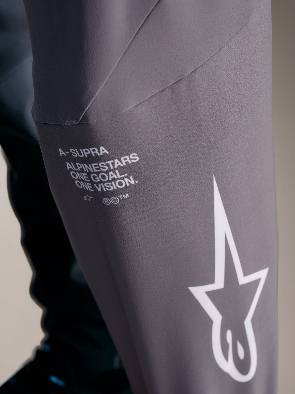 A-Supra Elite-broek in vervaagd grijs met witte Alpinestars-branding en het 'One Goal. One Vision.' race-motto.