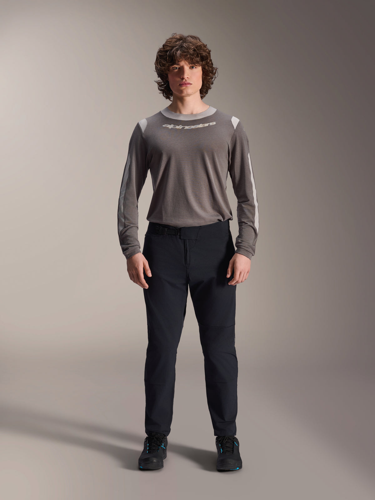 Alpinestars A-Dura Elite broek, zwarte mountainbikebroek, technische fietskleding met een normale pasvorm, gedragen met een grijze jersey met lange mouwen en zwarte schoenen, duurzame Cordura®-constructie voor off-road rijden