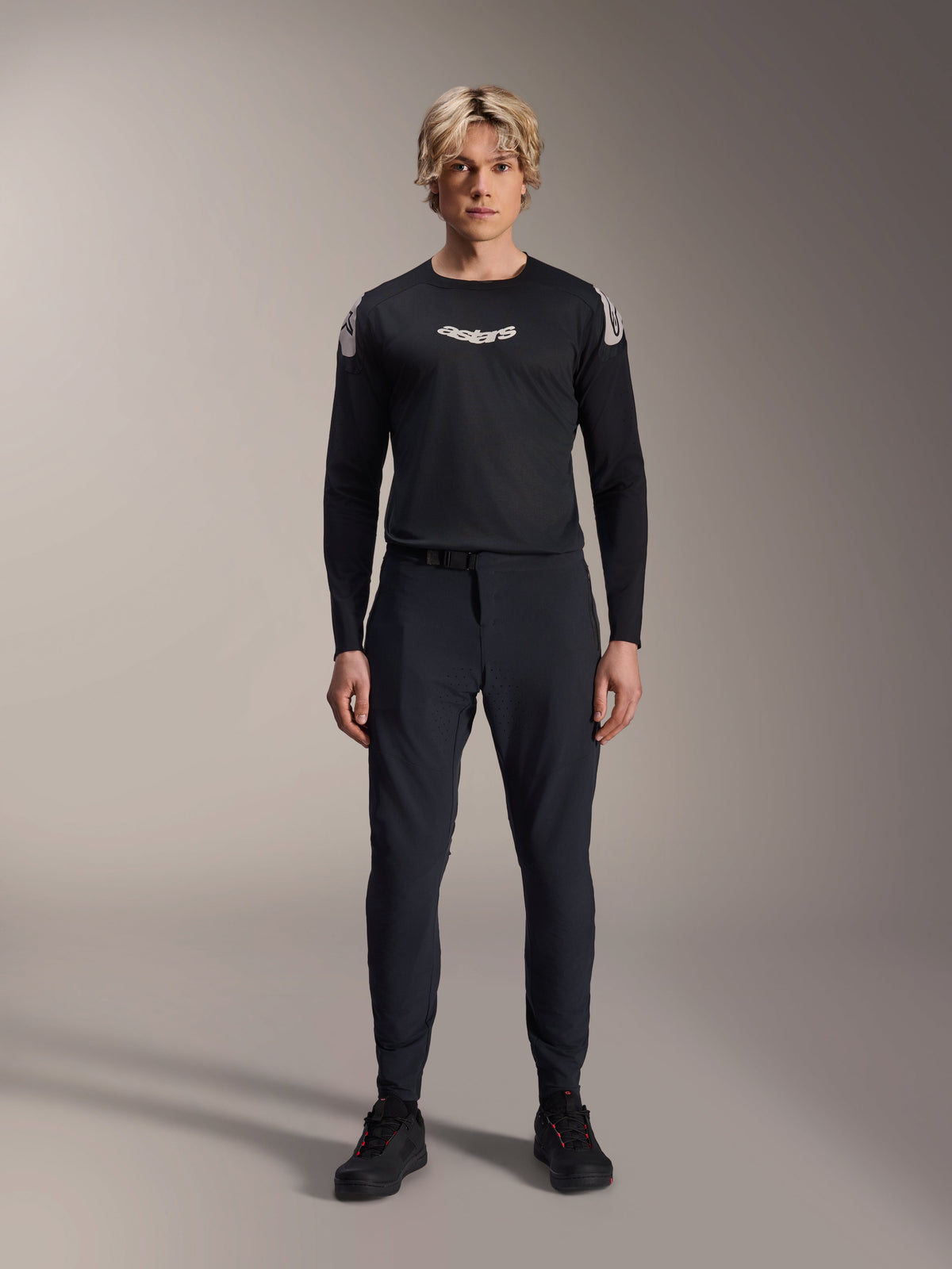 Male model wearing the Alpinestars A-Aria Polartec Elite Long Sleeve Jersey in Black, featuring a white Astars logo on the chest and shoulder branding, paired with black technical MTB pants and shoes, performance mountain bike gear