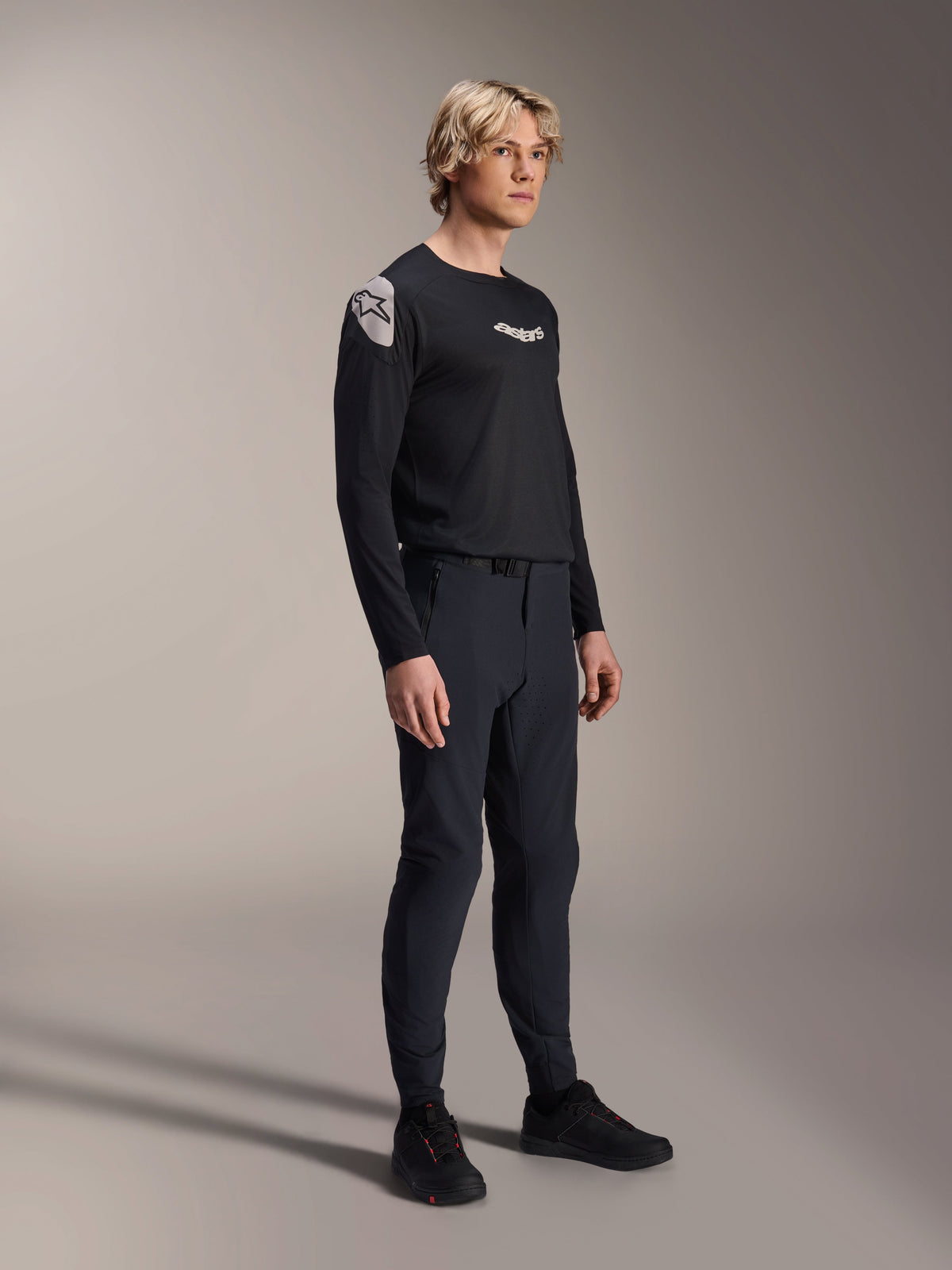 Model draagt Alpinestars A-Aria Polartec Elite Jersey met lange mouwen in het zwart, gecombineerd met een bijpassende zwarte technische mountainbikebroek en zwarte schoenen, prestatiegerichte fietskleding voor off-road rijden, studio-opname.