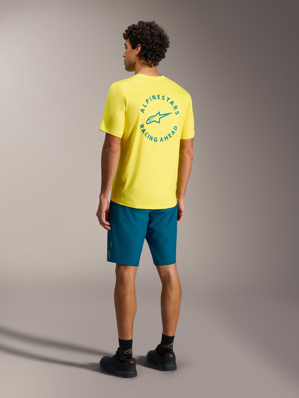 Blauwgroene Alpinestars A-Dura Ride shorts met een geel jersey, achteraanzicht van mountainbike-uitrusting.