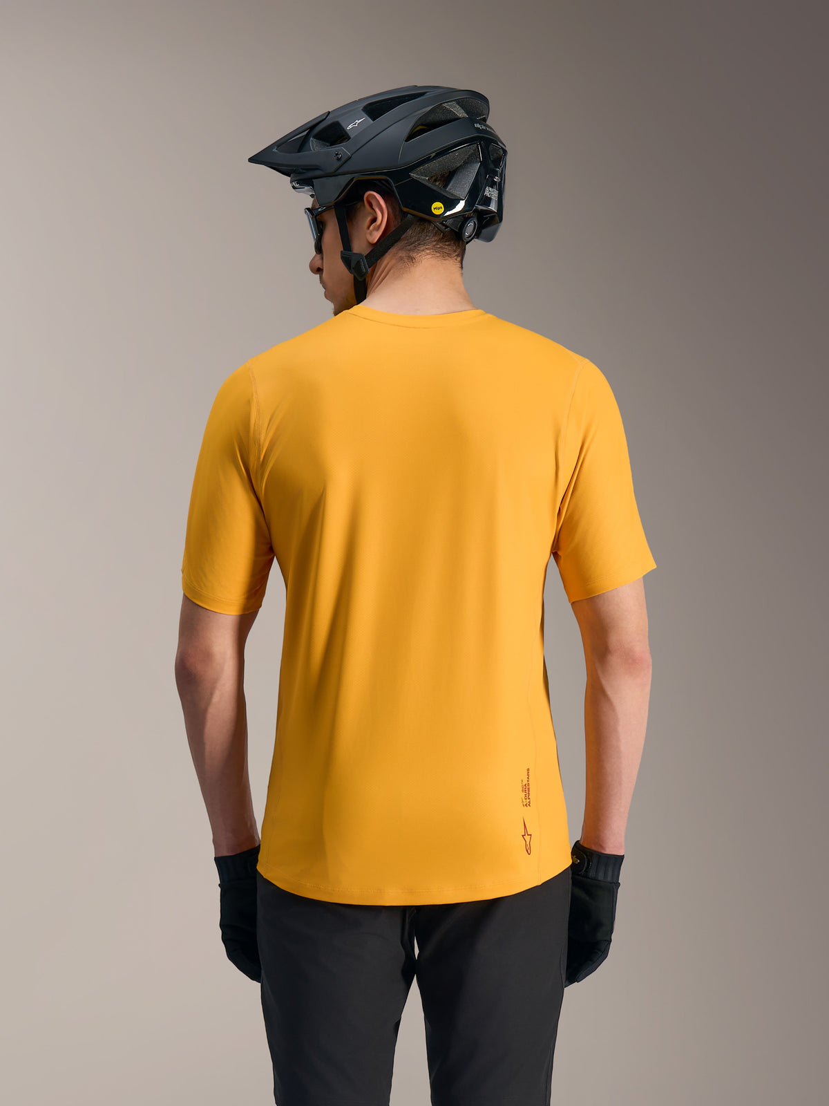 Oranje A-Dura Ride MTB-trui met korte mouwen, verlengde achterkant en logo, achteraanzicht met zwarte helm.