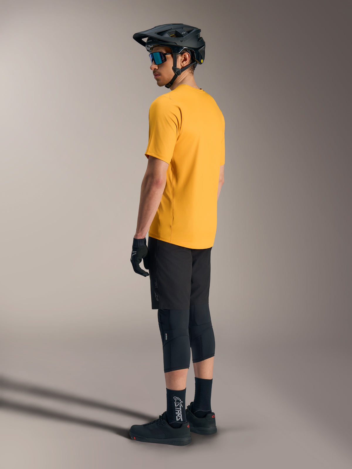 Alpinestars A-Dura Ride Jersey met korte mouwen in oranje, achteraanzicht op een rijder met zwarte MTB-gear en helm.