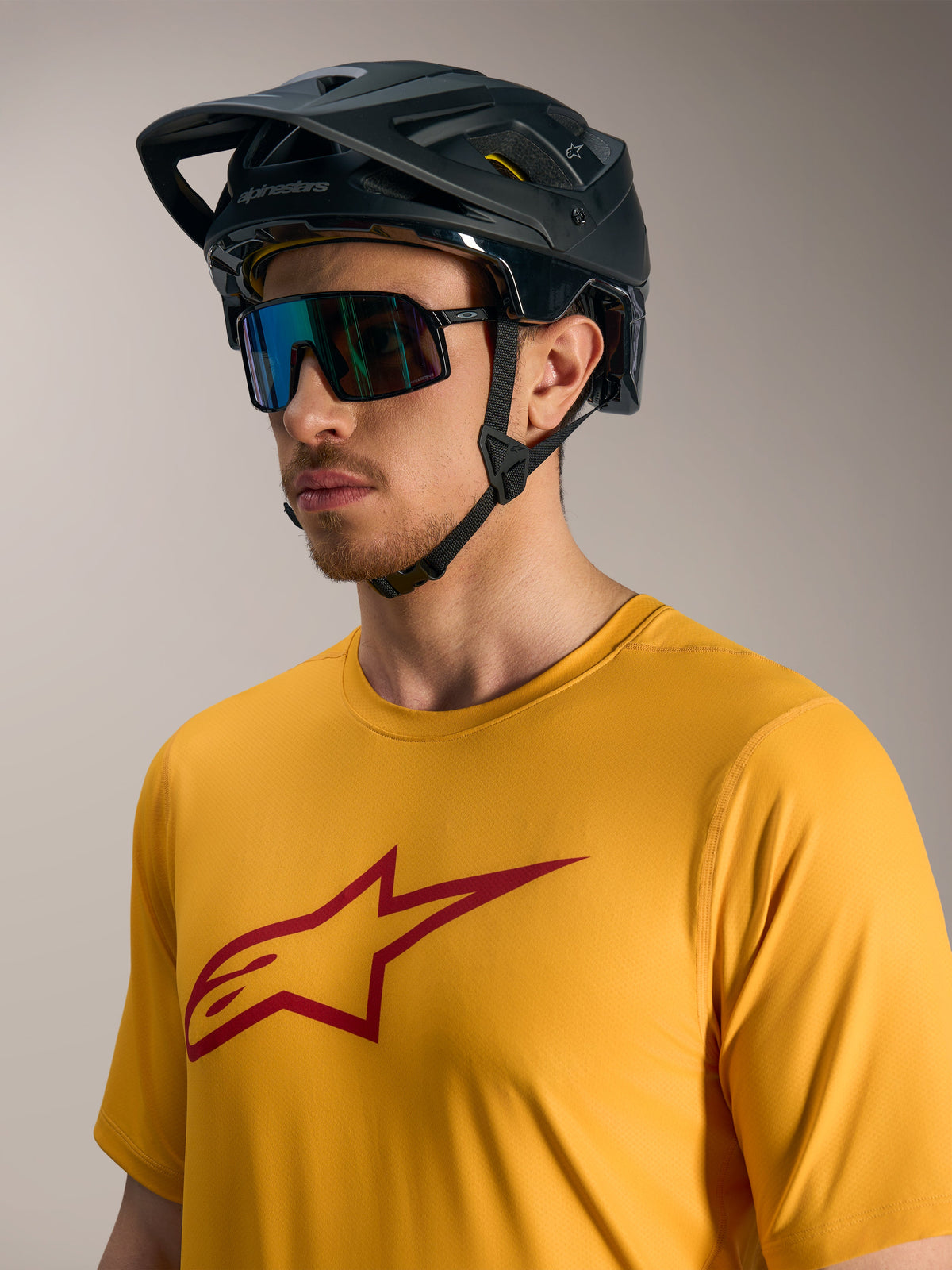 Oranje A-Dura Ride fietsshirt met korte mouwen, rood Astars-logo, zwarte MTB-helm en sportieve zonnebril.