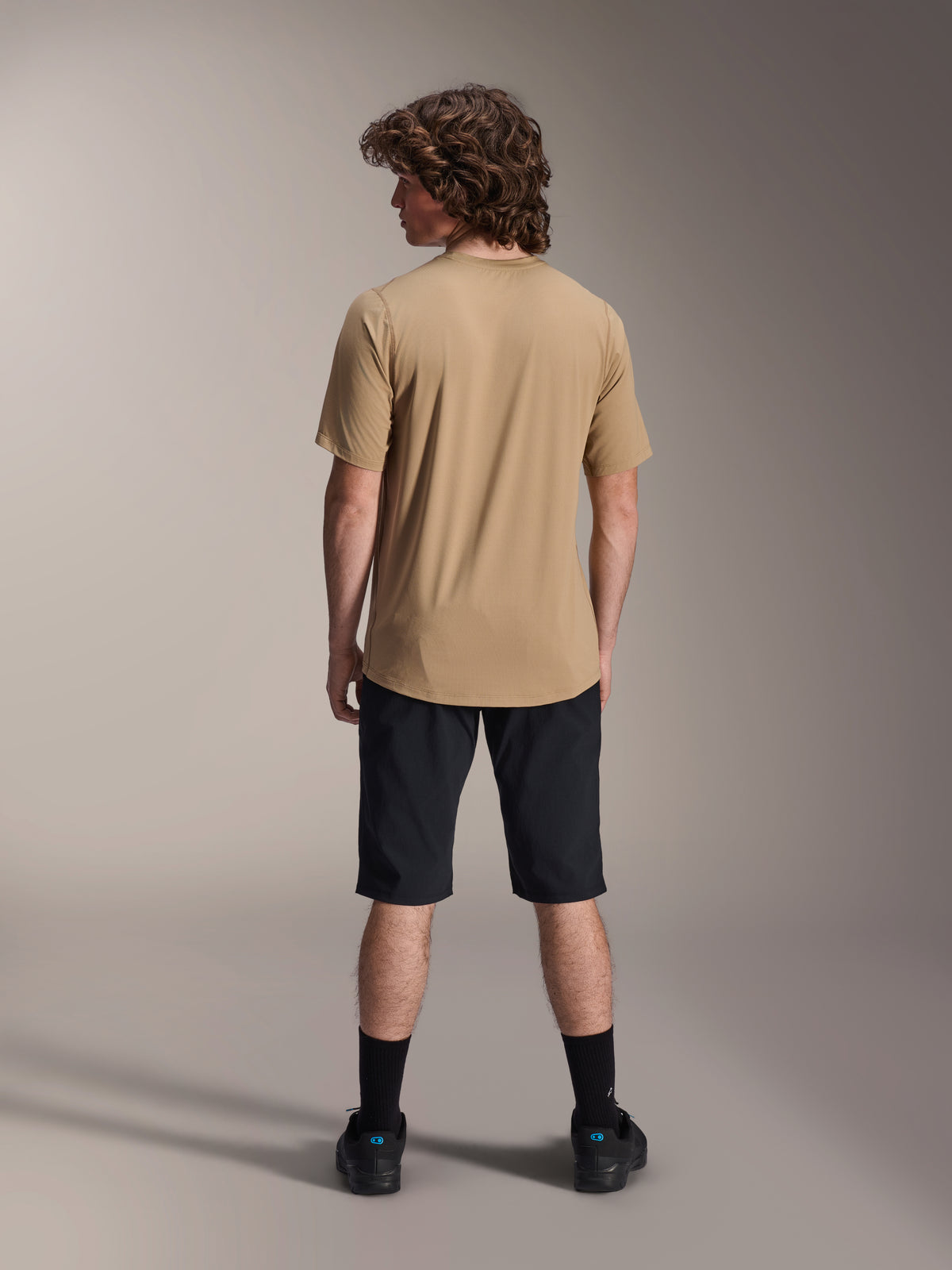Mannelijk model van achteren in een zwarte Alpinestars A-Dura Short en een beige A-Dura Short Sleeve Jersey, gecombineerd met zwarte sokken en mountainbikeschoenen, functionele MTB trail outfit