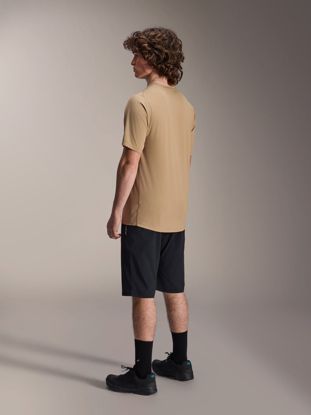 Alpinestars A-Dura Shorts, mountainbike short, zwart, gecombineerd met een beige A-Dura jersey met korte mouwen en zwarte fietsschoenen, normale pasvorm en duurzame constructie voor off-road fietsen, zij-achteraanzicht