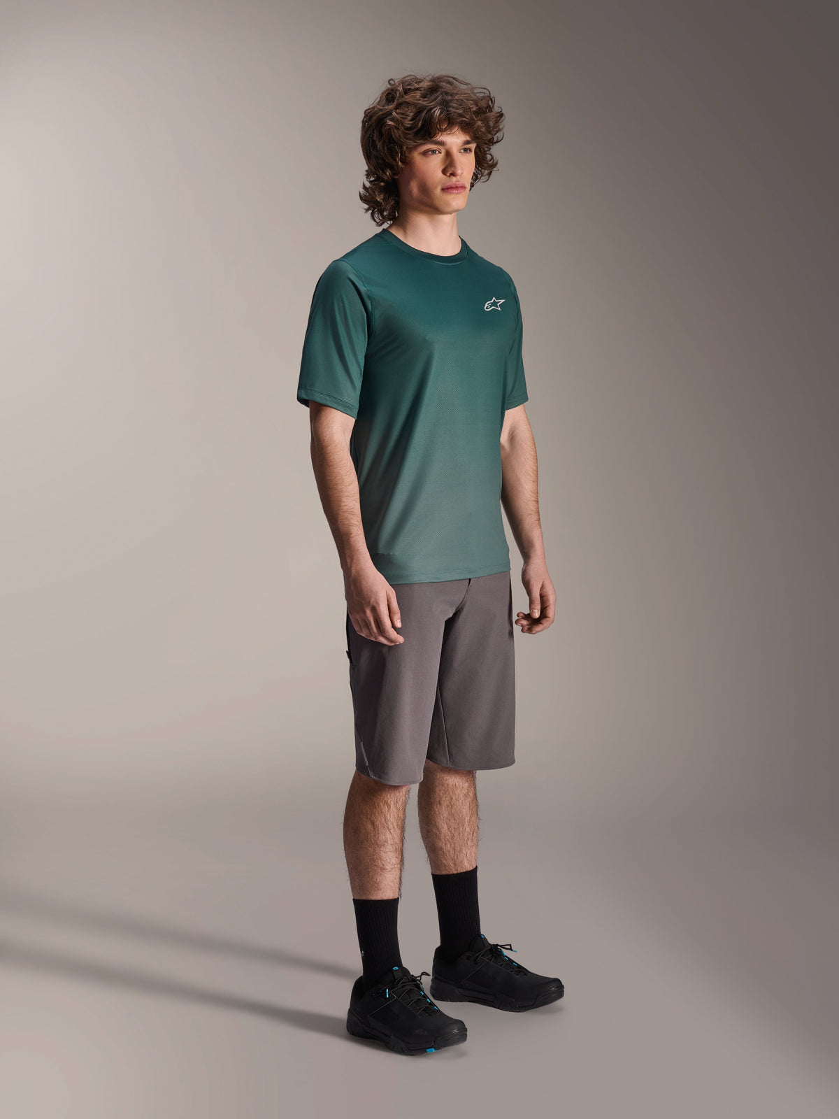 Alpinestars A-Dura Rise Jersey - Korte Mouwen in Silver Pine, groene mountainbike jersey gedragen door een model met grijze short en zwarte sneakers, casual MTB trail kleding met een klein wit logo op de borst