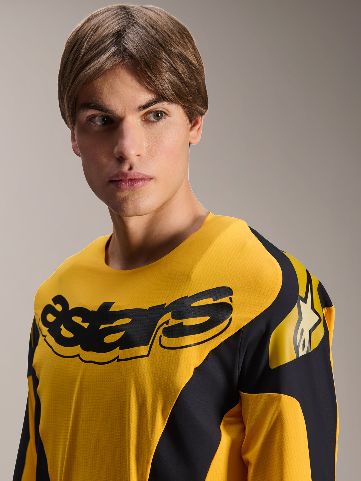Alpinestars Limited Edition A-Supra Melt Gold Jersey, MTB-jersey met lange mouwen, donkergeel met zwarte race-geïnspireerde graphics, met een zwart 'astars' woordmerk op de borst en ster-logo op de schouder, gedragen door een mannelijk model