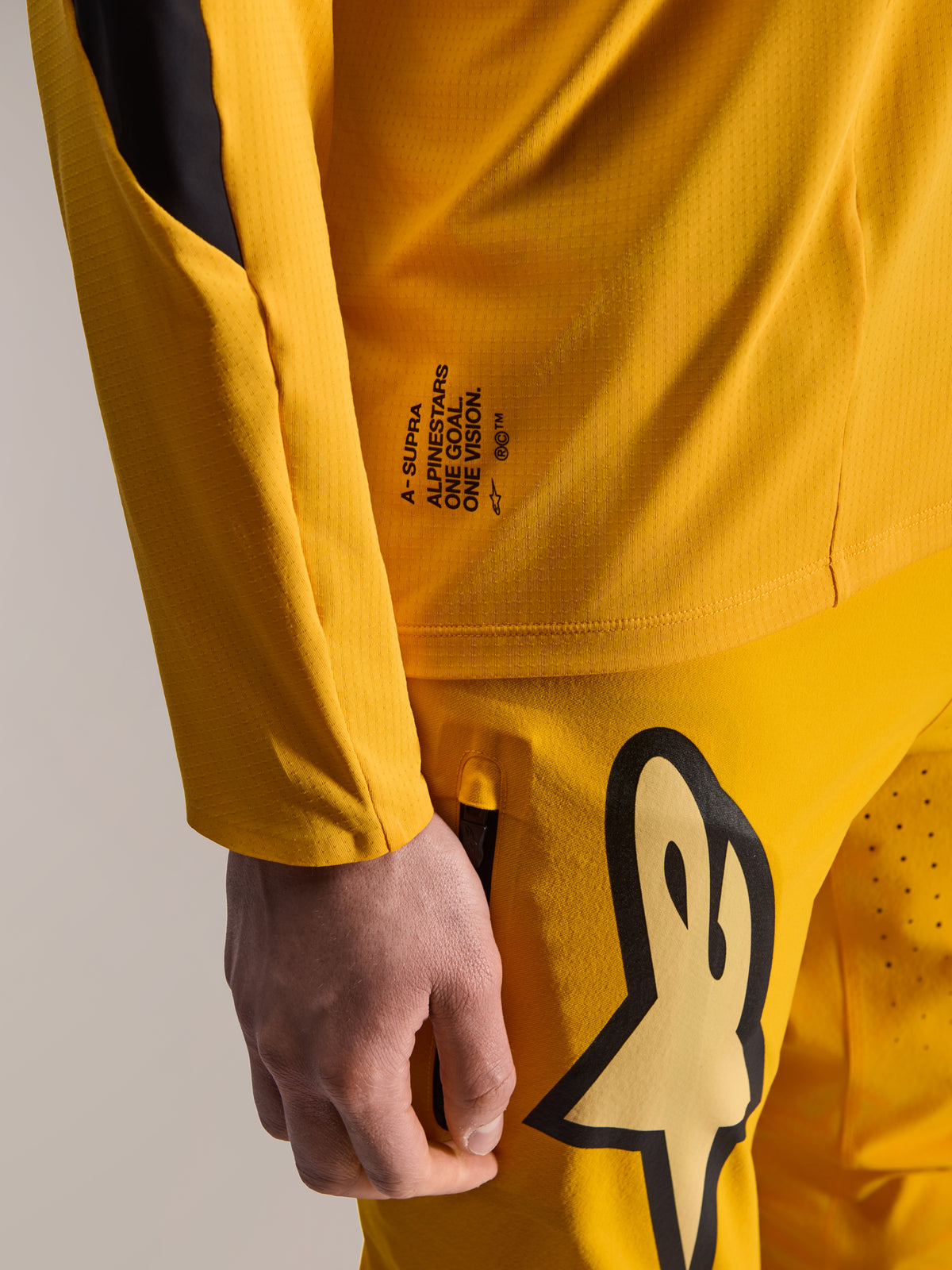 Alpinestars Limited Edition A-Supra Melt Gold Pants en bijpassende LS Jersey, donkergeel, close-up weergave met 'One Goal. One Vision.' branding en een groot gestileerd logo op de dij, hoogwaardige MTB-uitrusting