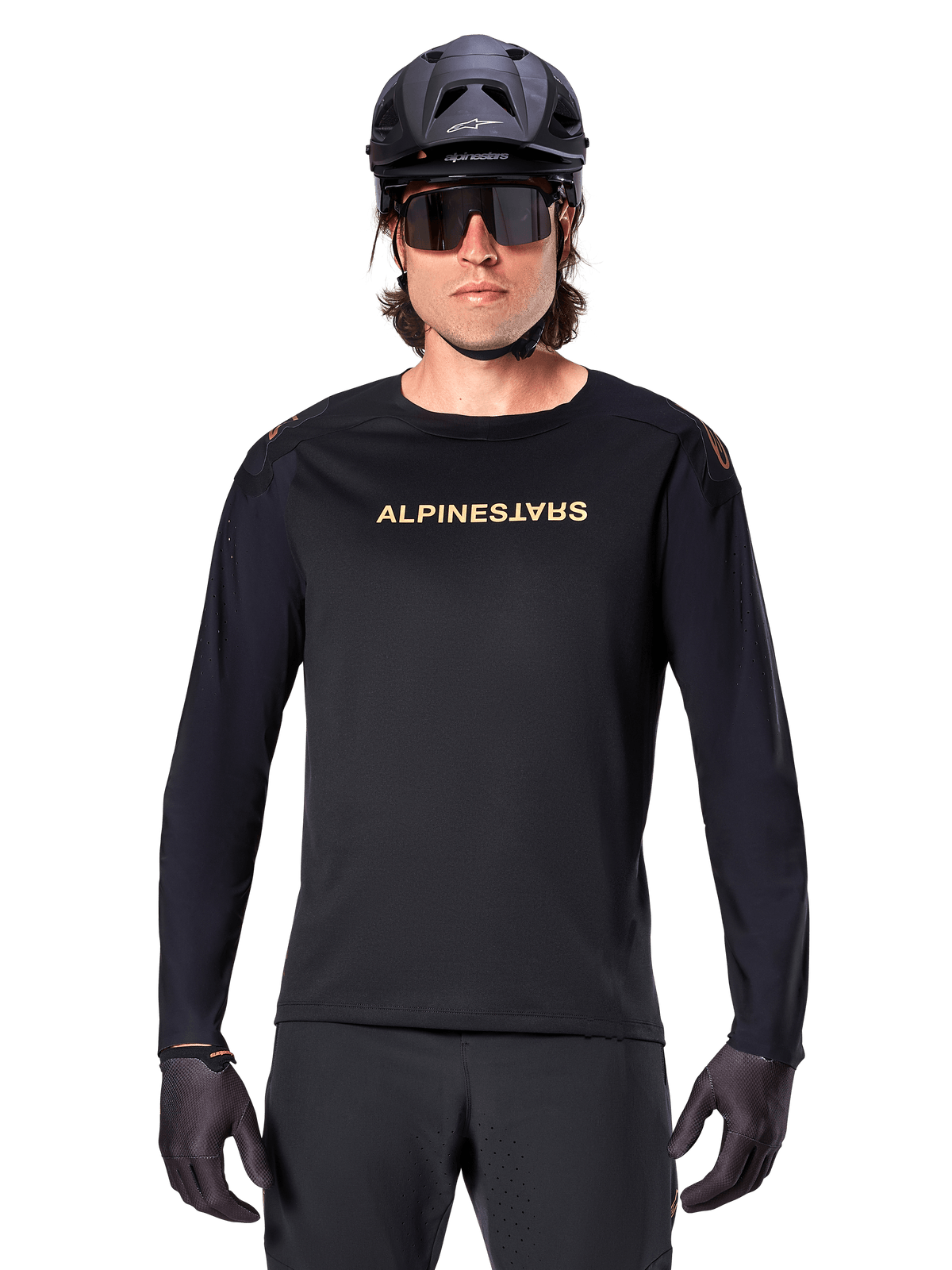 Alpinestars A-Aria Polartec Switch Jersey met lange mouwen, zwart, goudkleurig Alpinestars-logo op de borst, gedragen met een zwarte MTB-helm, donkere zonnebril en zwarte handschoenen, professionele mountainbike trailuitrusting