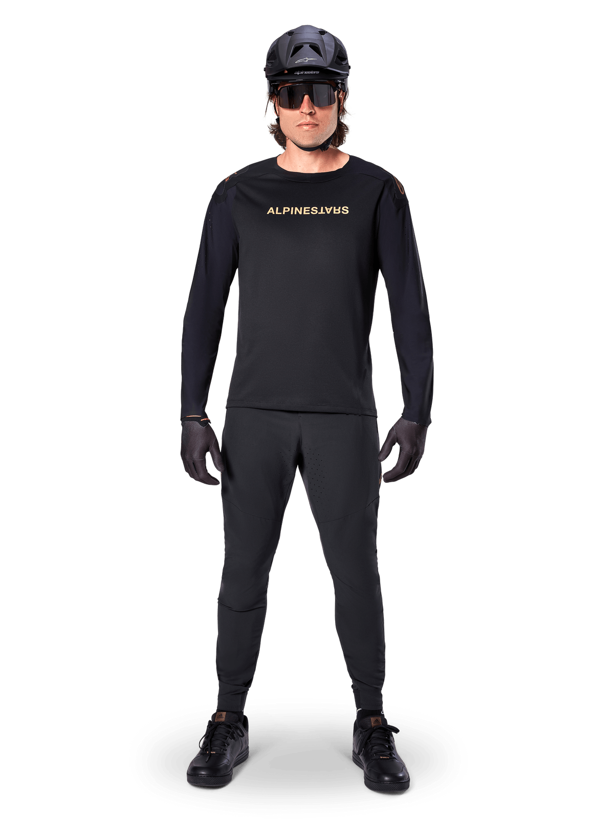 Alpinestars A-Aria Polartec Switch Jersey met lange mouwen, zwart, gedragen door een rijder met bijpassende zwarte technische broek, zwarte helm, zonnebril en zwarte handschoenen, performance MTB-uitrusting voor off-road paden