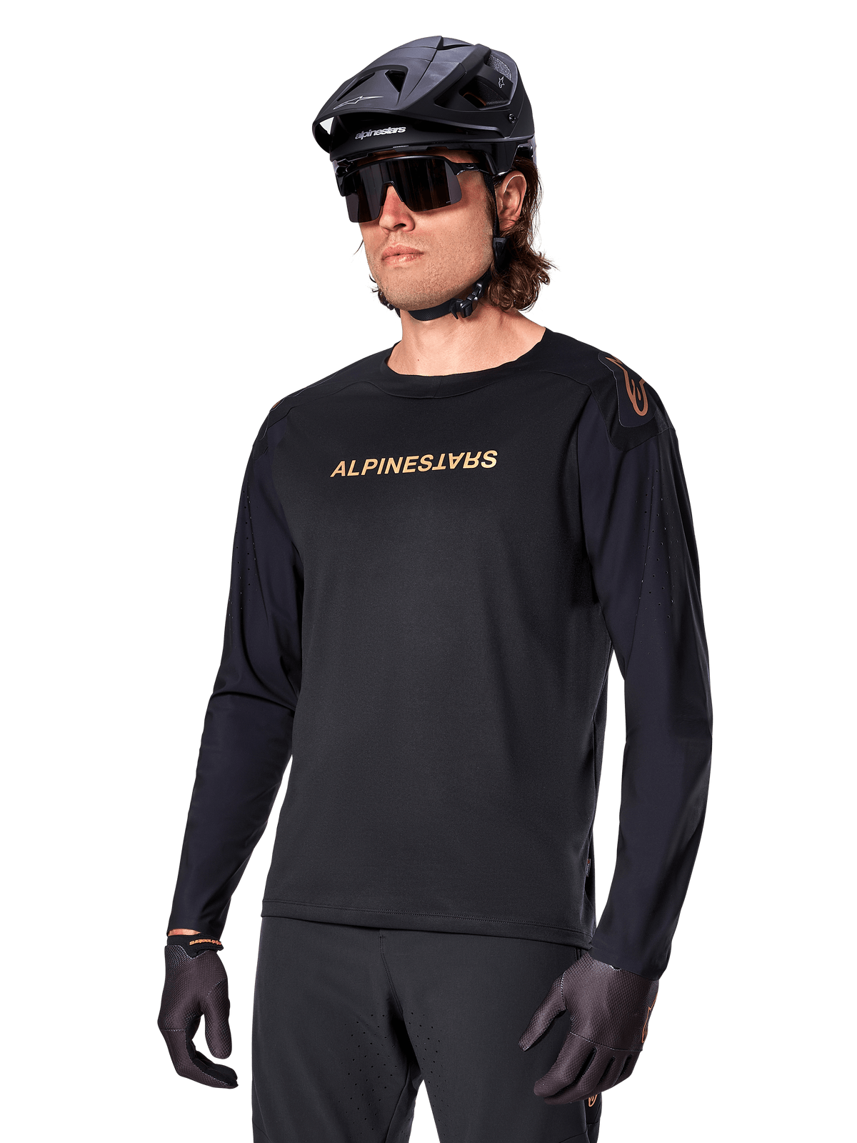 Alpinestars A-Aria Polartec Switch fietsshirt met lange mouwen, zwart met goudkleurig logo, MTB mountainbike-kleding, gedragen met een zwarte helm en zonnebril, met lasergesneden ventilatie op de mouwen en vochtafvoerende Polartec-stof voor off-road prestaties