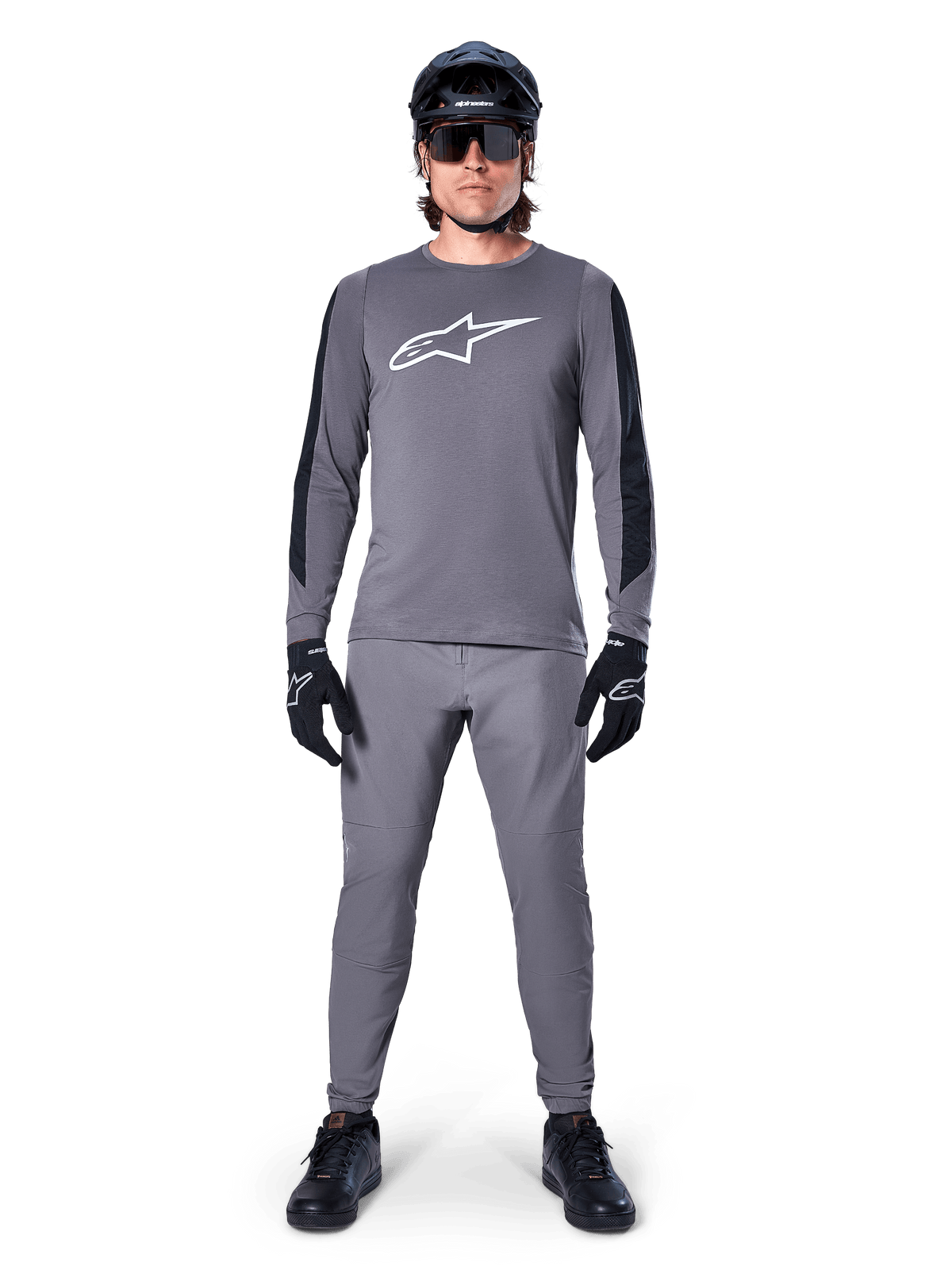 Alpinestars A-Dura Dri Astar Jersey, Long Sleeve MTB Jersey in Dark Gray, featuring a white chest logo and black sleeve panels, worn with matching gray pants, black helmet, sunglasses, and gloves for a complete off-road cycling outfit