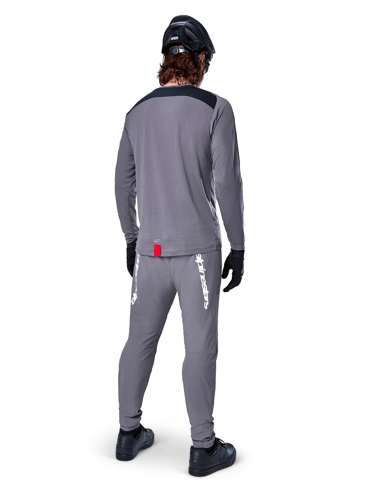 Alpinestars A-Dura Dri Astar Jersey - Long Sleeve, Dark Gray, back view of rider wearing matching pants and black helmet, features black shoulder panels and a small red tag at the hem, technical off-road cycling gear