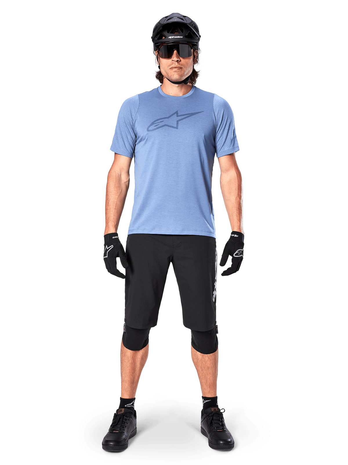 Mannelijke mountainbiker die het Alpinestars A-Dura Dri Astar fietsshirt met korte mouwen in Infinity Blue draagt, voorzien van een prominent Astars-logo op de borst, gecombineerd met een zwarte MTB-short, zwarte helm, zonnebril en beschermende uitrusting voor off-road rijden