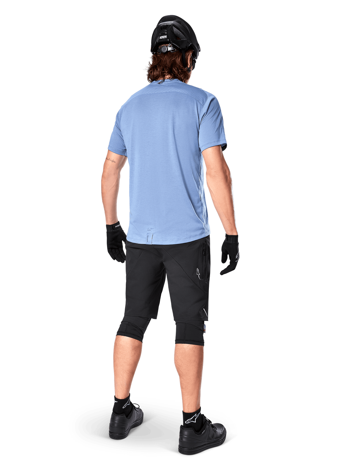 Alpinestars A-Dura Dri Astar jersey met korte mouwen, Infinity Blue, achteraanzicht, gecombineerd met een zwarte mountainbikeshort en helm, technische fietskleding met vochtafvoerende stof en een langere dropstaart