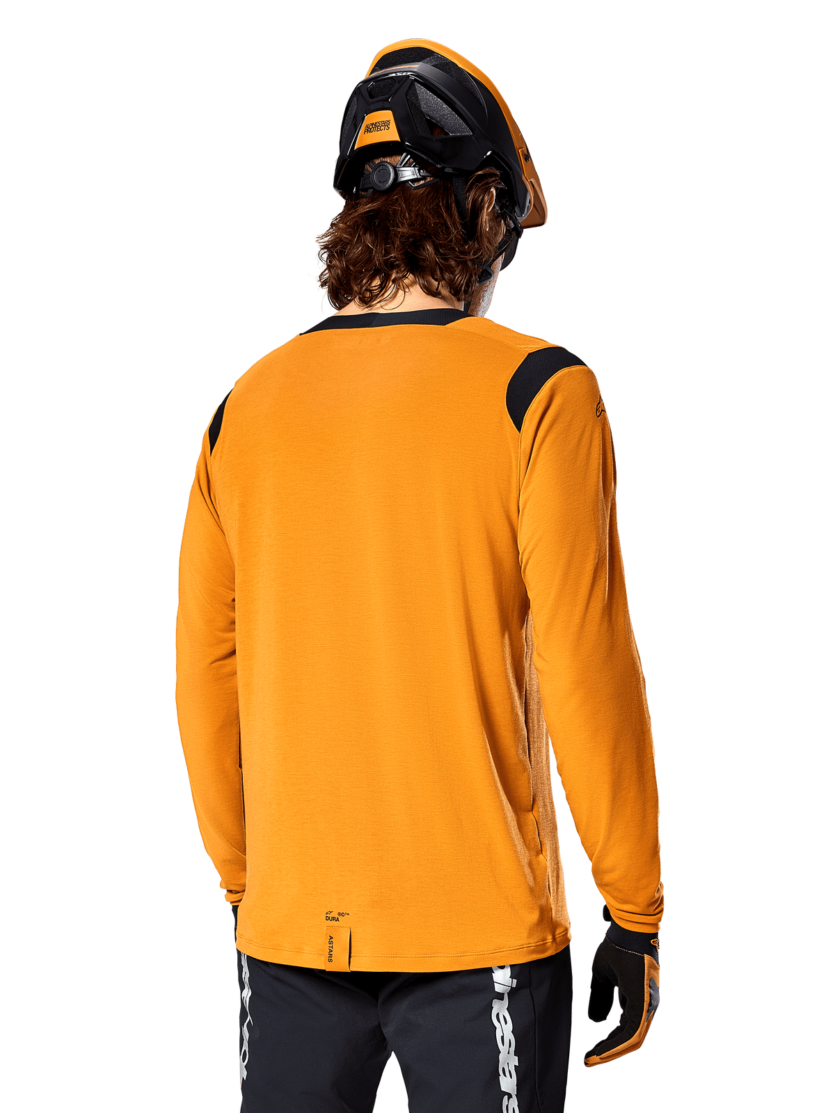 Alpinestars A-Dura Dri Wool Jersey met lange mouwen in Dark Gold, achteraanzicht van een rijder met mountainbikehelm en handschoenen, voorzien van zwarte mesh-panelen op de schouders en een verlengde achterzijde, technische fietskleding voor trailrijden