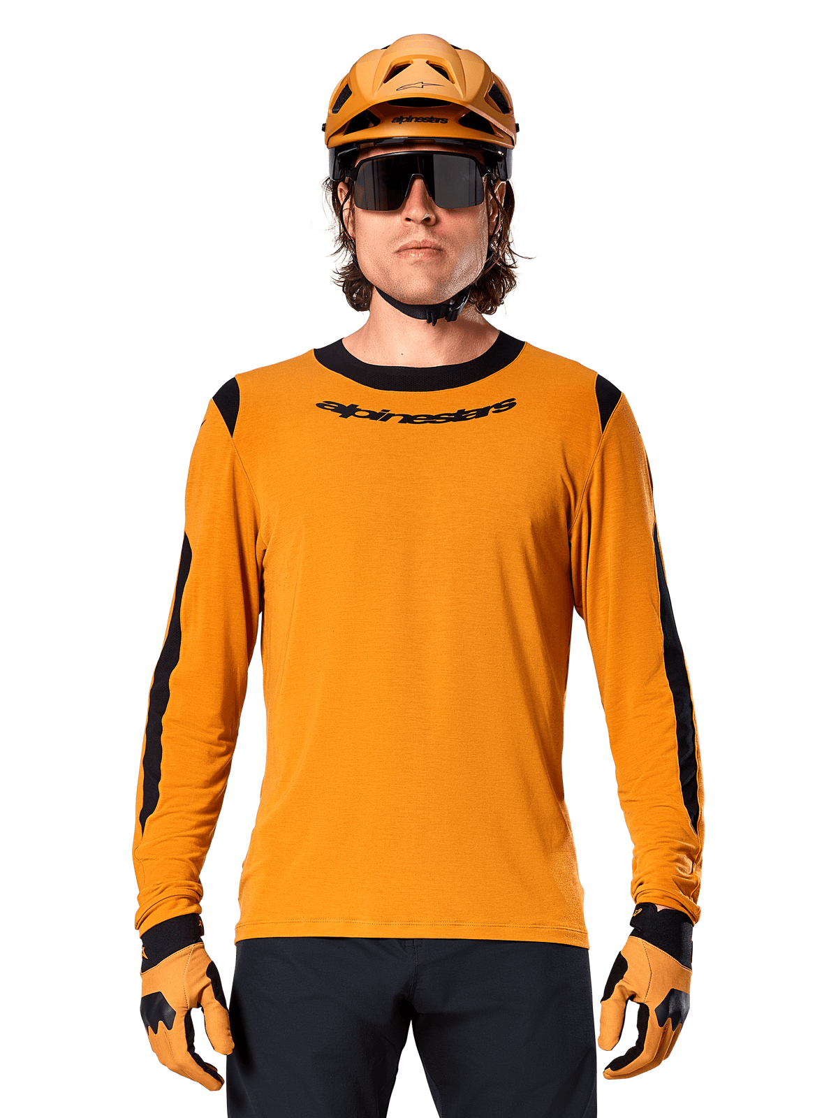Mannelijk model draagt Alpinestars A-Dura Dri Wool Jersey met lange mouwen in Dark Gold, gecombineerd met een bijpassende gouden MTB-helm en handschoenen, zwarte mesh panelen op schouders en mouwen, zwart Alpinestars-woordmerk op de borst, donkere zonnebril en broek, technische mountainbikekleding