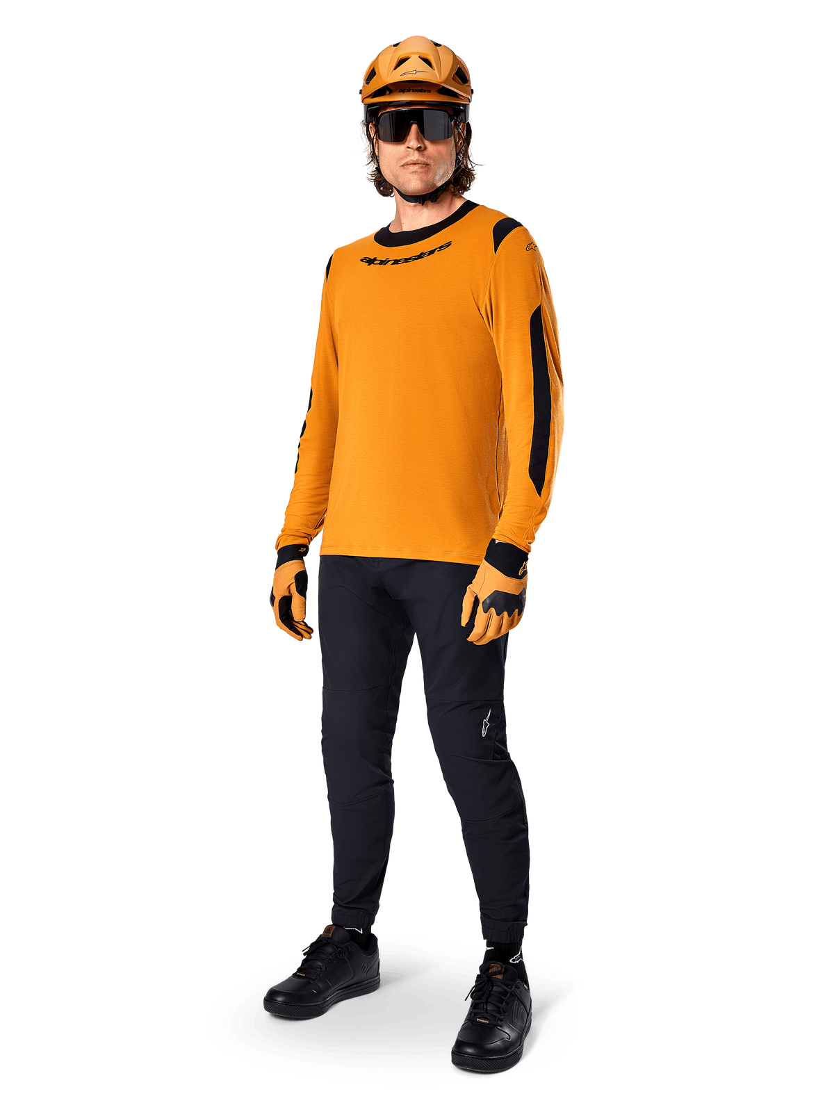 Alpinestars A-Dura Dri Wool Jersey - lange mouwen, donkergoud, gedragen met bijpassende oranje helm, zwarte MTB-broek en geel-zwarte handschoenen, volledige fietsoutfit voor off-road trailrijden