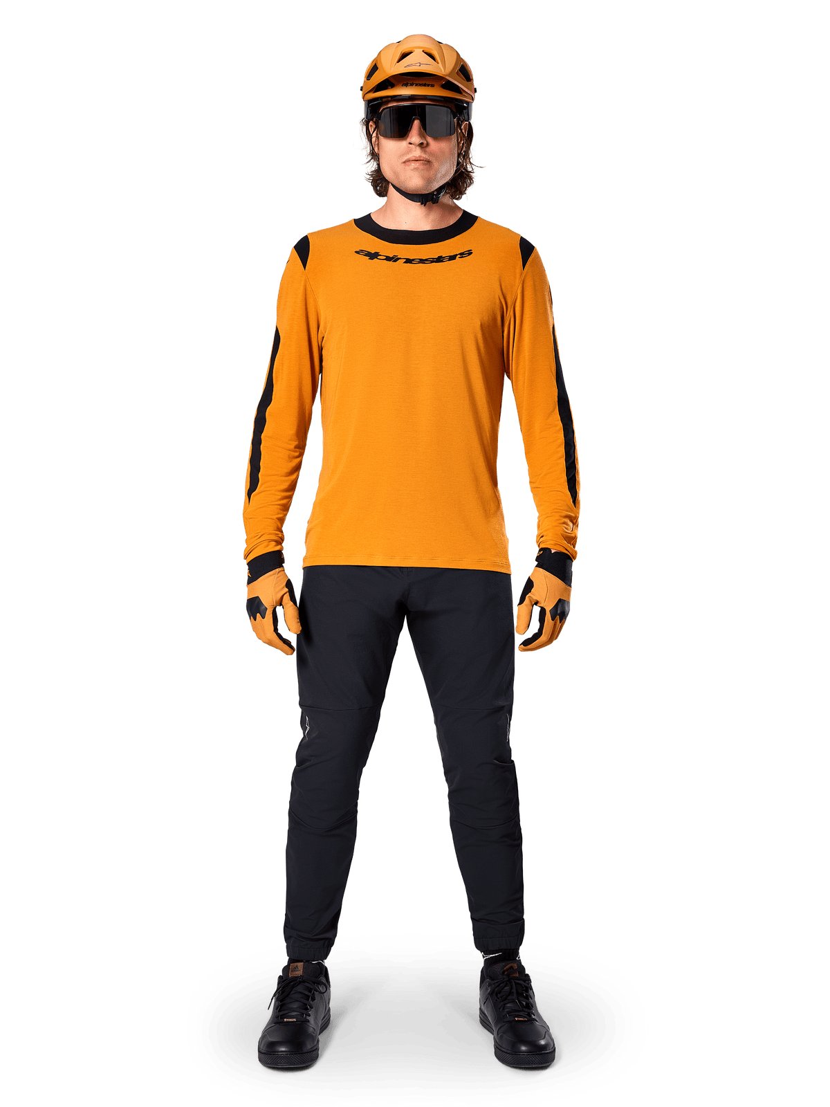 Mountainbiker met Alpinestars A-Dura Dri Wool jersey met lange mouwen, donkergoud met zwarte accenten op de kraag en mouwen, gecombineerd met een zwarte broek, bijpassende gouden helm, handschoenen en zwarte zonnebril, professionele mountainbike-uitrusting