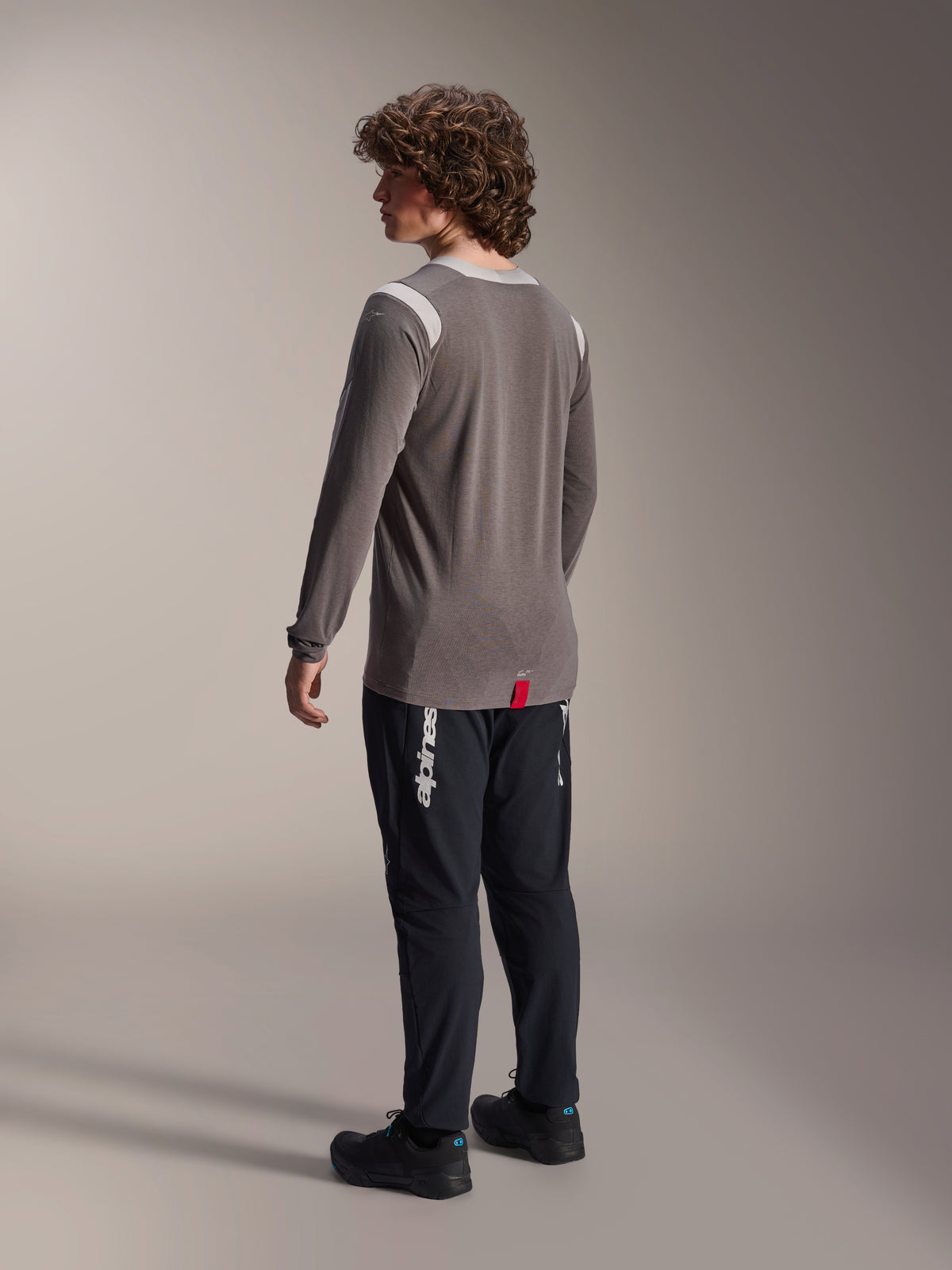 Alpinestars A-Dura Dri-Wool jersey met lange mouwen in grijs, gecombineerd met zwarte A-Dura Elite broek, achteraanzicht van model, wit Alpinestars-logo op de broekspijp, technische mountainbikekleding voor off-road ritten