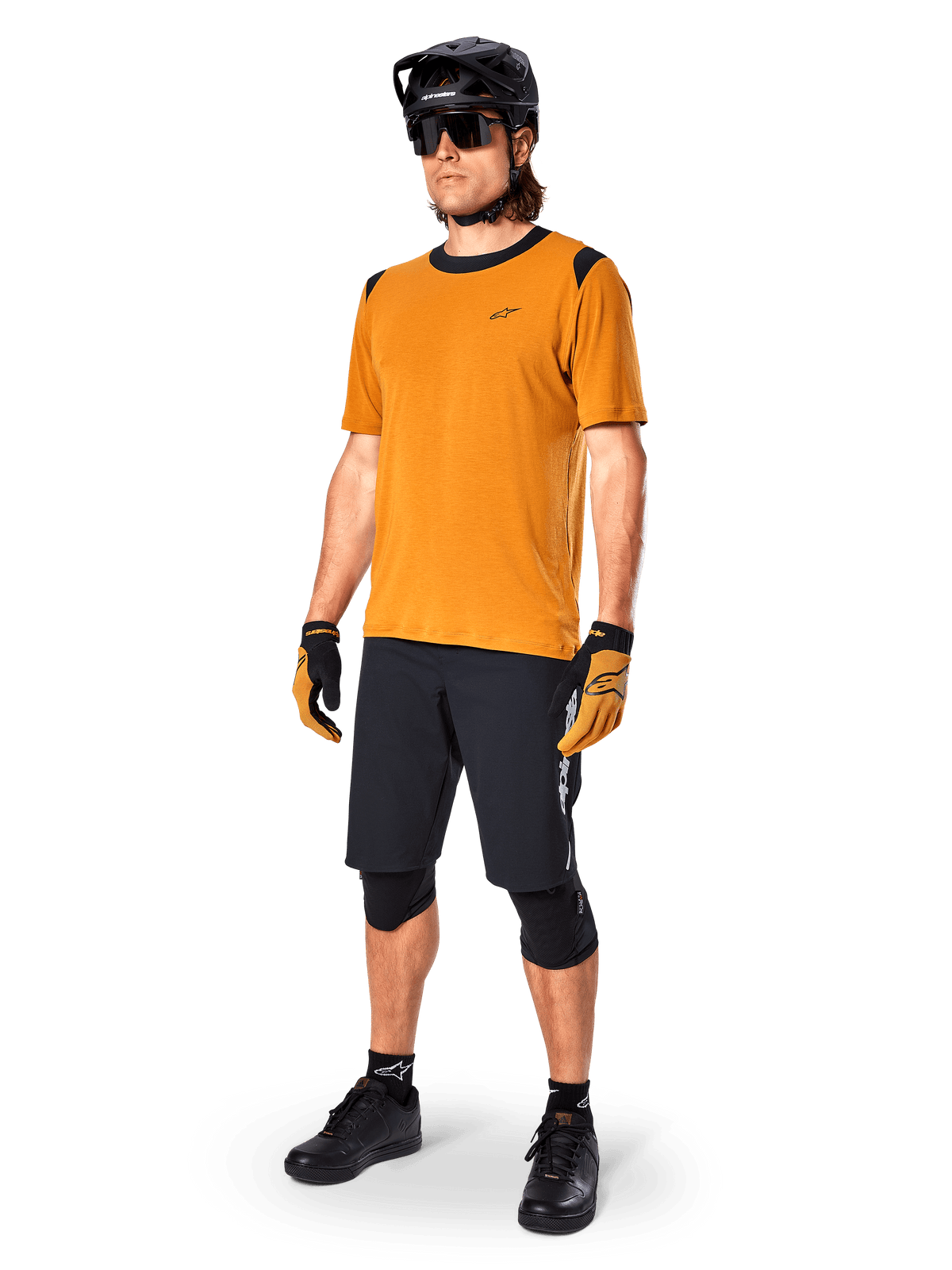 Mannelijk model in Alpinestars A-Dura Dri Wool Jersey met korte mouwen in Dark Gold, mountainbike-jersey met zwarte schouder- en kraagaccenten, gecombineerd met een zwarte MTB-short, zwarte helm en zonnebril, technische off-road fietsuitrusting