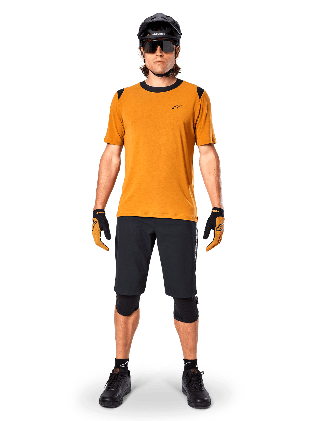Alpinestars A-Dura Dri Wool jersey met korte mouwen in Dark Gold, mountainbike-jersey gedragen met zwarte short en beschermende uitrusting, mosterdgele stof met zwarte kraag- en schouderaccenten, technische fietskleding voor trailrijden.