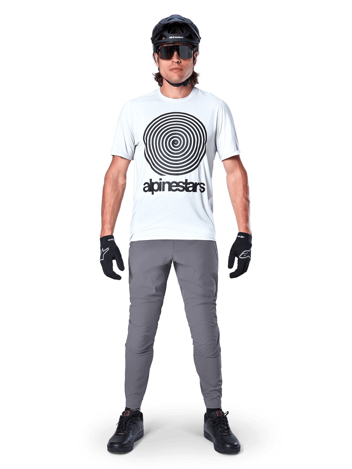 Mountain biker wearing Alpinestars A-Dura Oscar Jersey, Short Sleeve, White Dove with large black spiral logo, paired with grey pants, black helmet, sunglasses, and black gloves, performance MTB trail riding gear