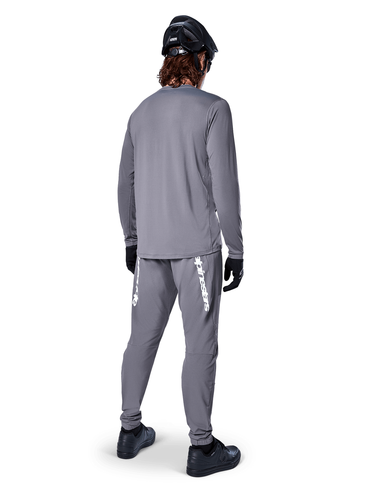 Alpinestars A-Dura Rocker Jersey met lange mouwen, donkergrijs, achteraanzicht van model met bijpassende grijze MTB-broek, zwarte helm en zwarte handschoenen, professioneel ontwerp voor mountainbikekleding