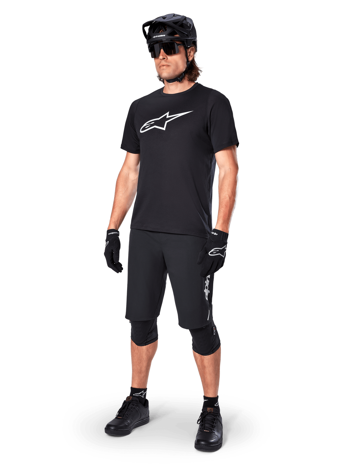 Mountainbiker draagt het Alpinestars A-Dura Dri Oscar fietsshirt met korte mouwen in Black Reflective, voorzien van een groot wit logo op de borst, gecombineerd met bijpassende zwarte MTB-short, handschoenen en helm, technische fietskleding voor off-road prestaties
