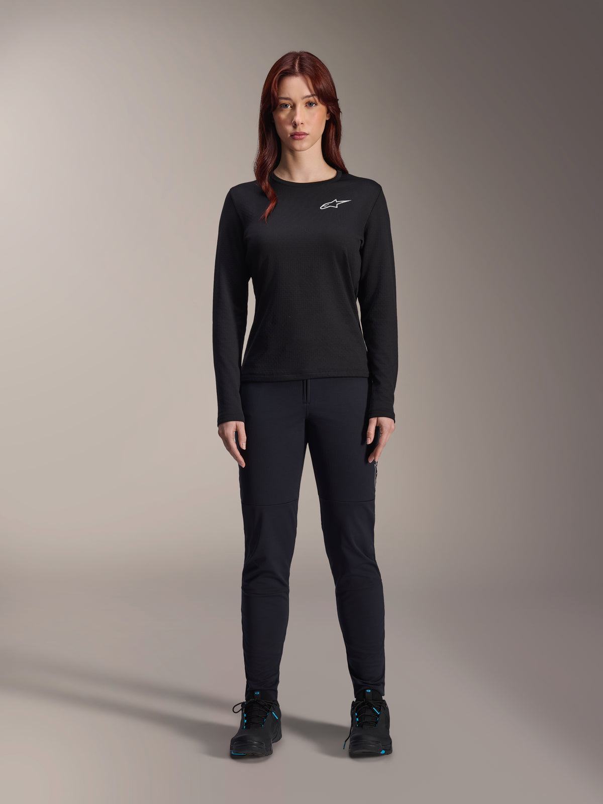 Alpinestars Stella A-Dura Thermal Jersey, dames mountainbike jersey met lange mouwen in het zwart, voorzien van een wit logo op de borst, gedragen met bijpassende zwarte uitrusting en fietsschoenen, studioportret.