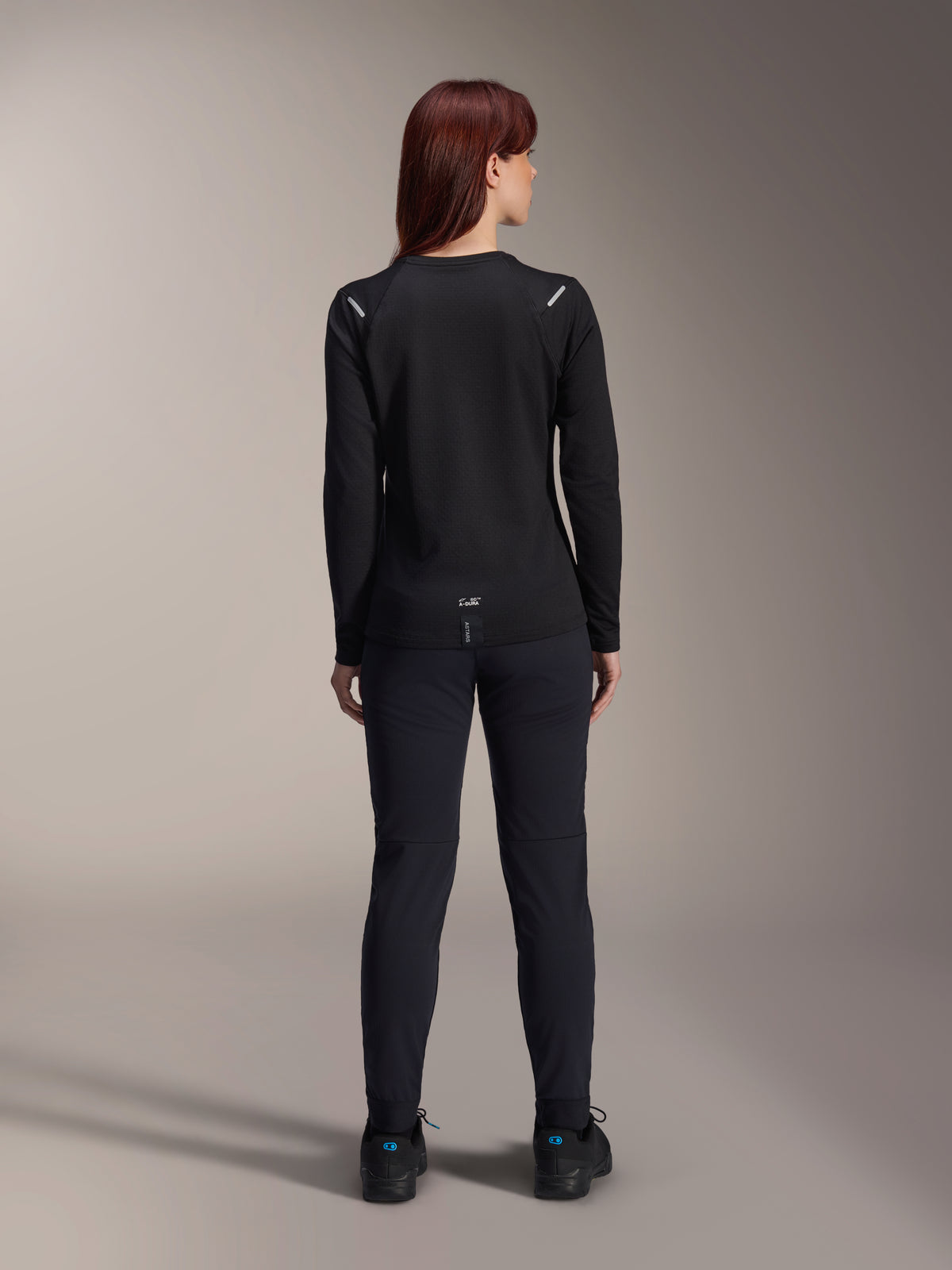 Alpinestars Stella A-Dura Thermal Jersey voor dames, achteraanzicht, zwart, fietsshirt met lange mouwen en geïsoleerd fleece, gedragen met bijpassende zwarte broek en schoenen, met kleine A-Dura branding op de onderrug en reflecterende schouderaccenten, speciaal ontworpen voor MTB-ritten voor dames.