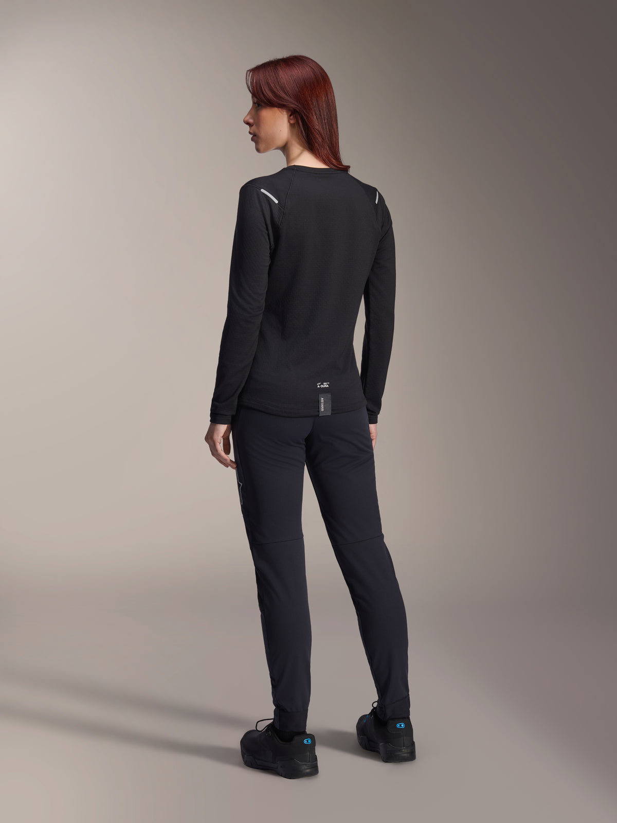Alpinestars Stella A-Dura Thermal Jersey voor dames, MTB-shirt met lange mouwen in het zwart, achteraanzicht met reflecterende schouderaccenten en verlengde drop tail, gedragen met zwarte broek en schoenen, performance kleding voor mountainbiken