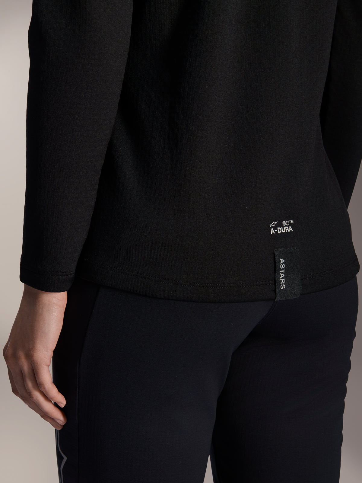 Alpinestars Stella A-Dura Thermal Jersey voor dames, zwart thermisch MTB-shirt, close-up van de onderste zoom aan de achterkant met witte A-DURA-branding en verticaal ASTARS-logolabel, ontworpen voor mountainbiken in koud weer